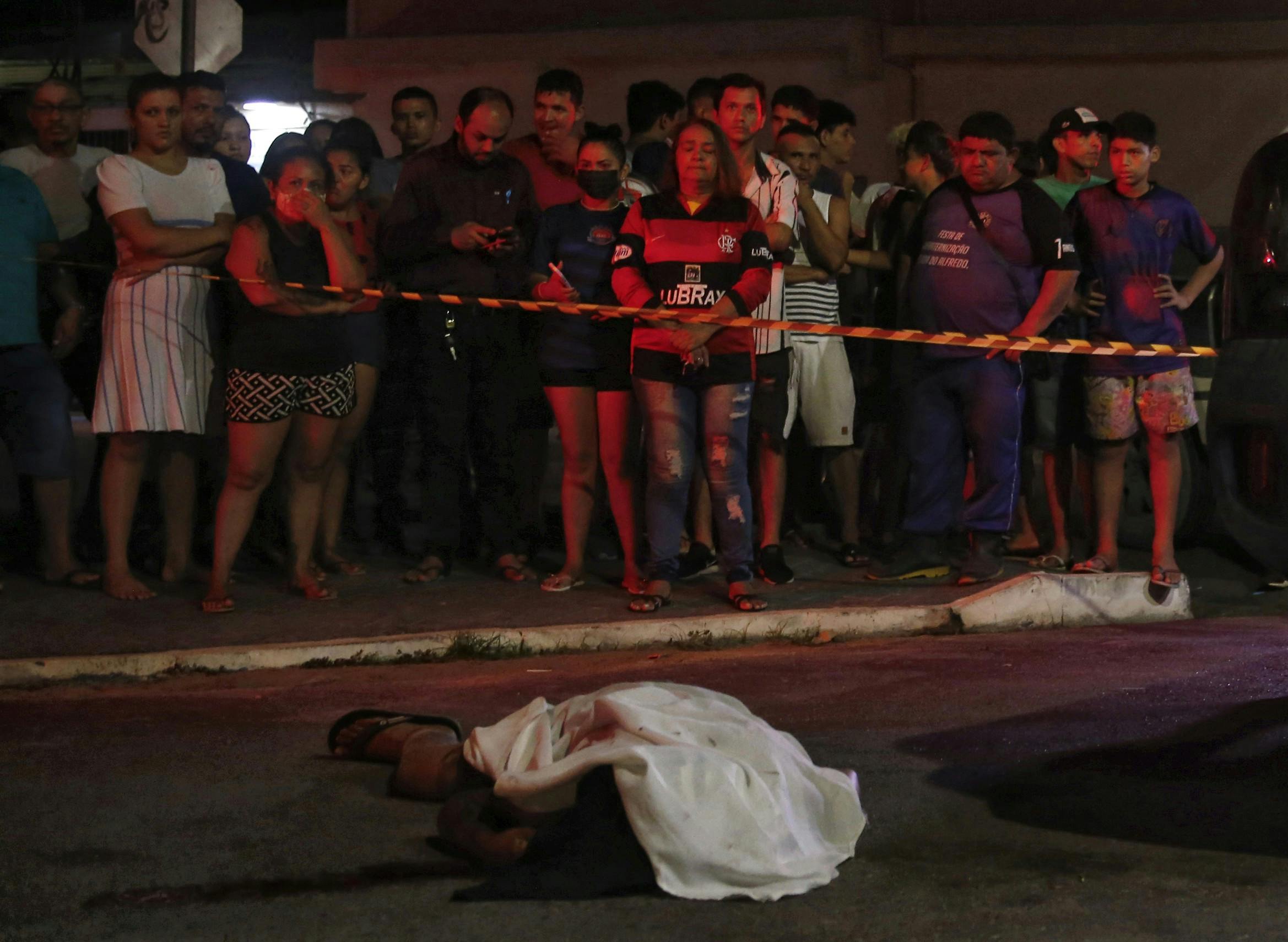 Naboer står bag afspærring og ser på liget af en skudt mand i Brasilien