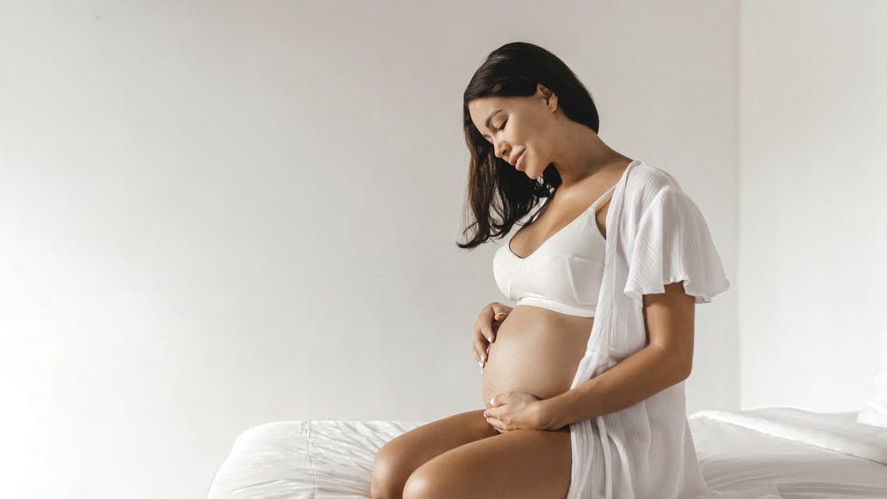 Mørkhåret gravid kvinde på seng