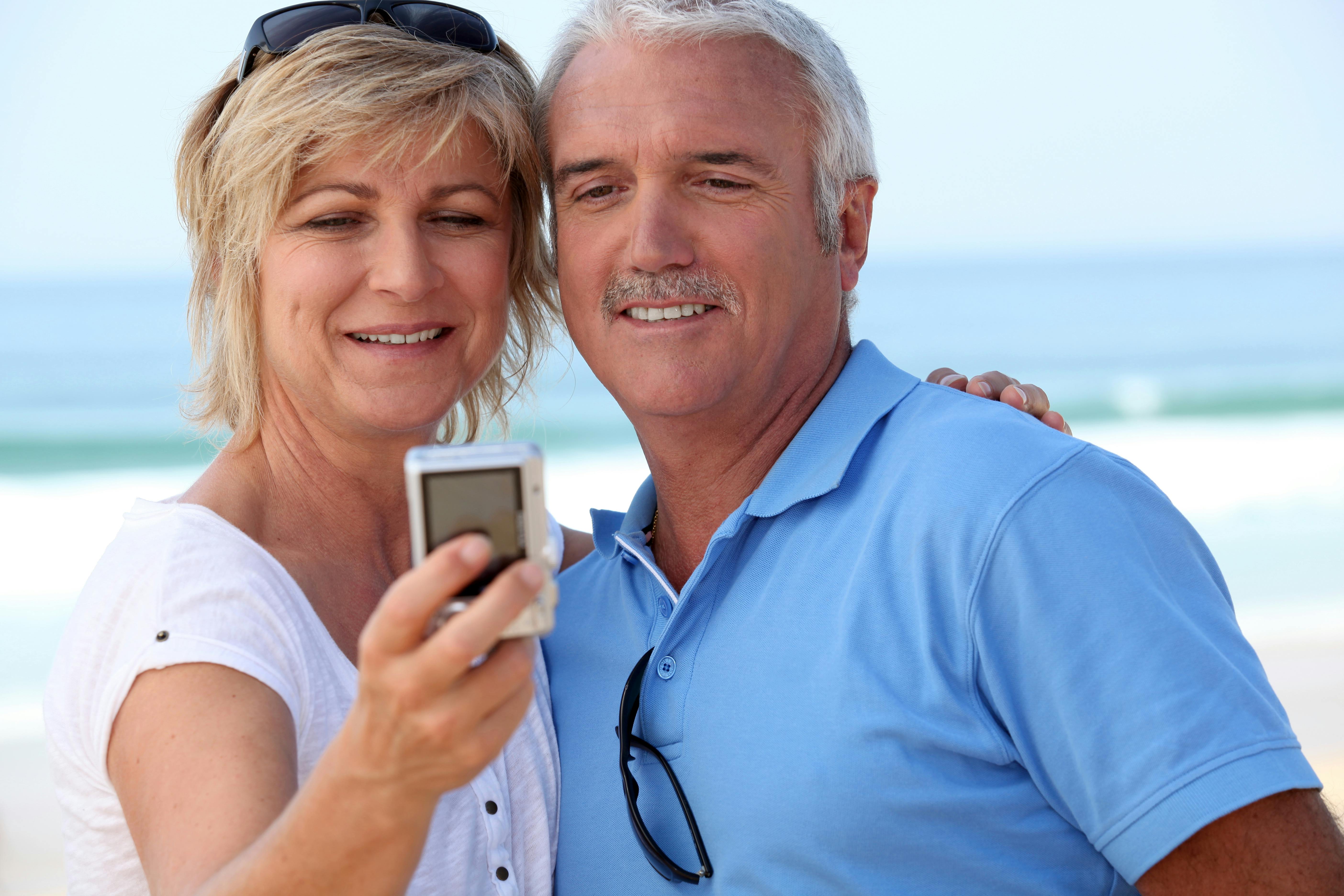 Forelsket midaldrende par tager en selfie på stranden med havet i baggrunden