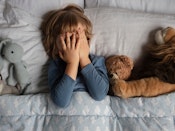 Dreng på 6-7 år ligger i sin seng og holder hænderne for øjnene. Han er omgivet at sine bamser.