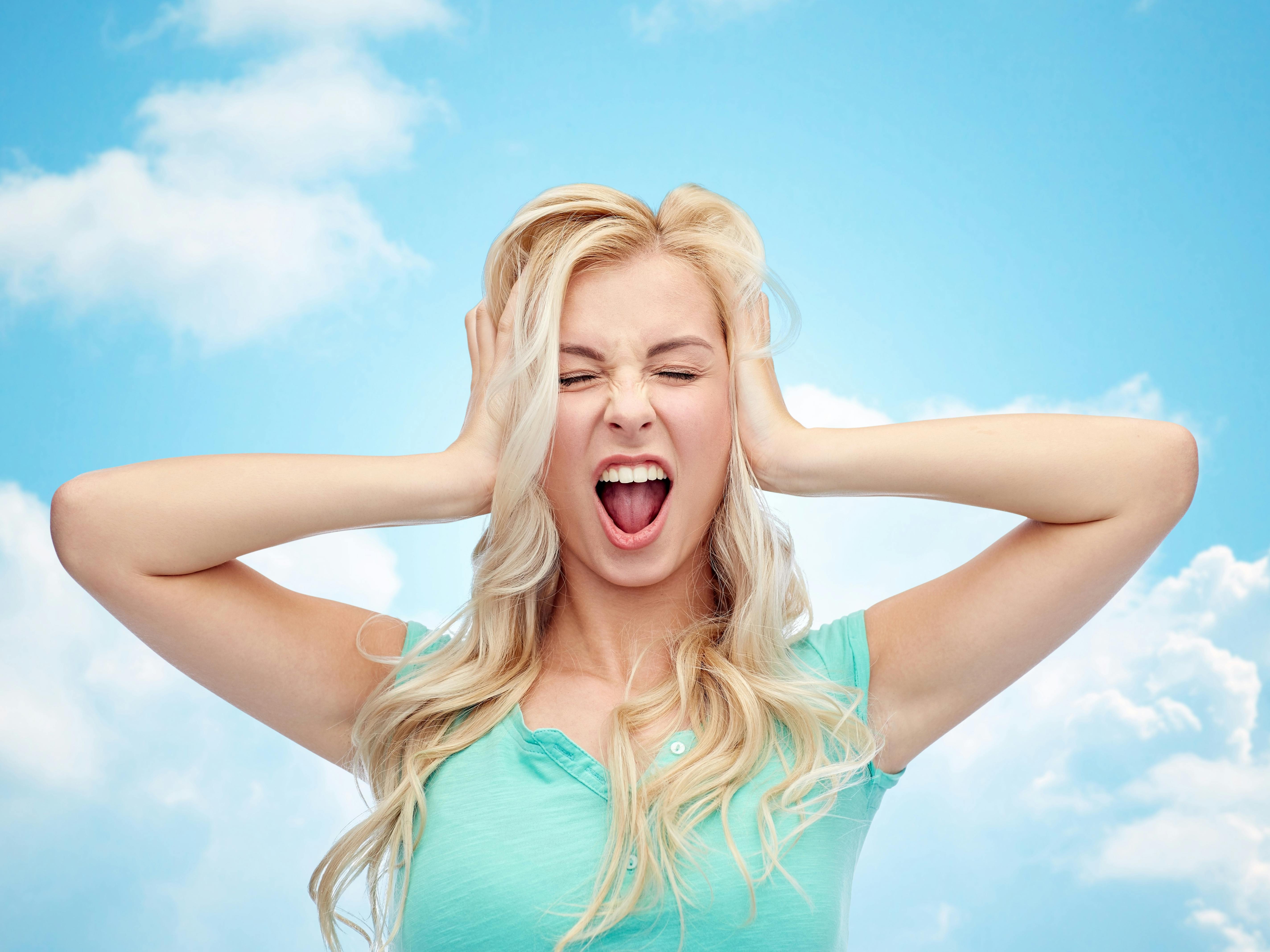 emotions, expressions, stress and people concept - young woman holding to her head and screaming over blue sky and clouds background
