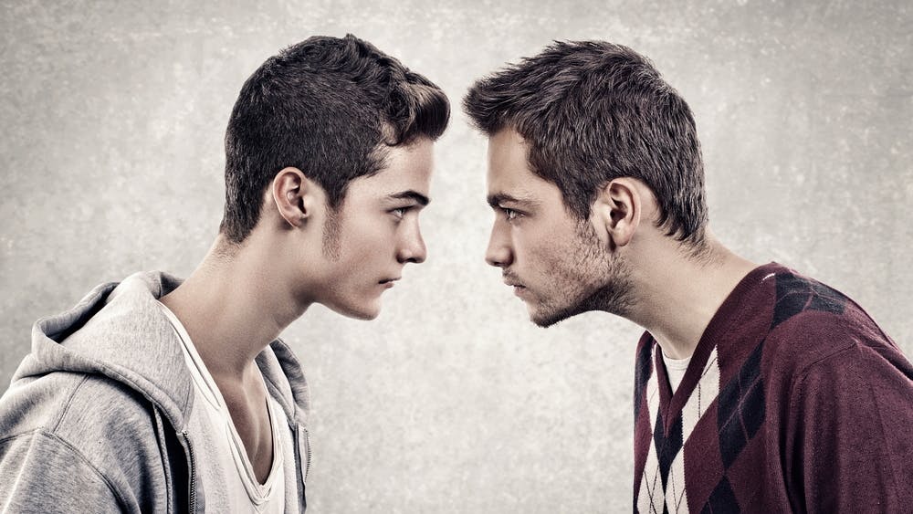 To unge mænd står med hovederne tæt sammen og ser rasende ud.
