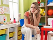 Ung kvinde sidder og så en skammel i en børnehave. Hun ser trist ud.