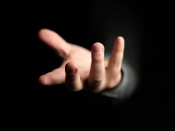 En hånd rækker ud fra en helt mørk baggrund
