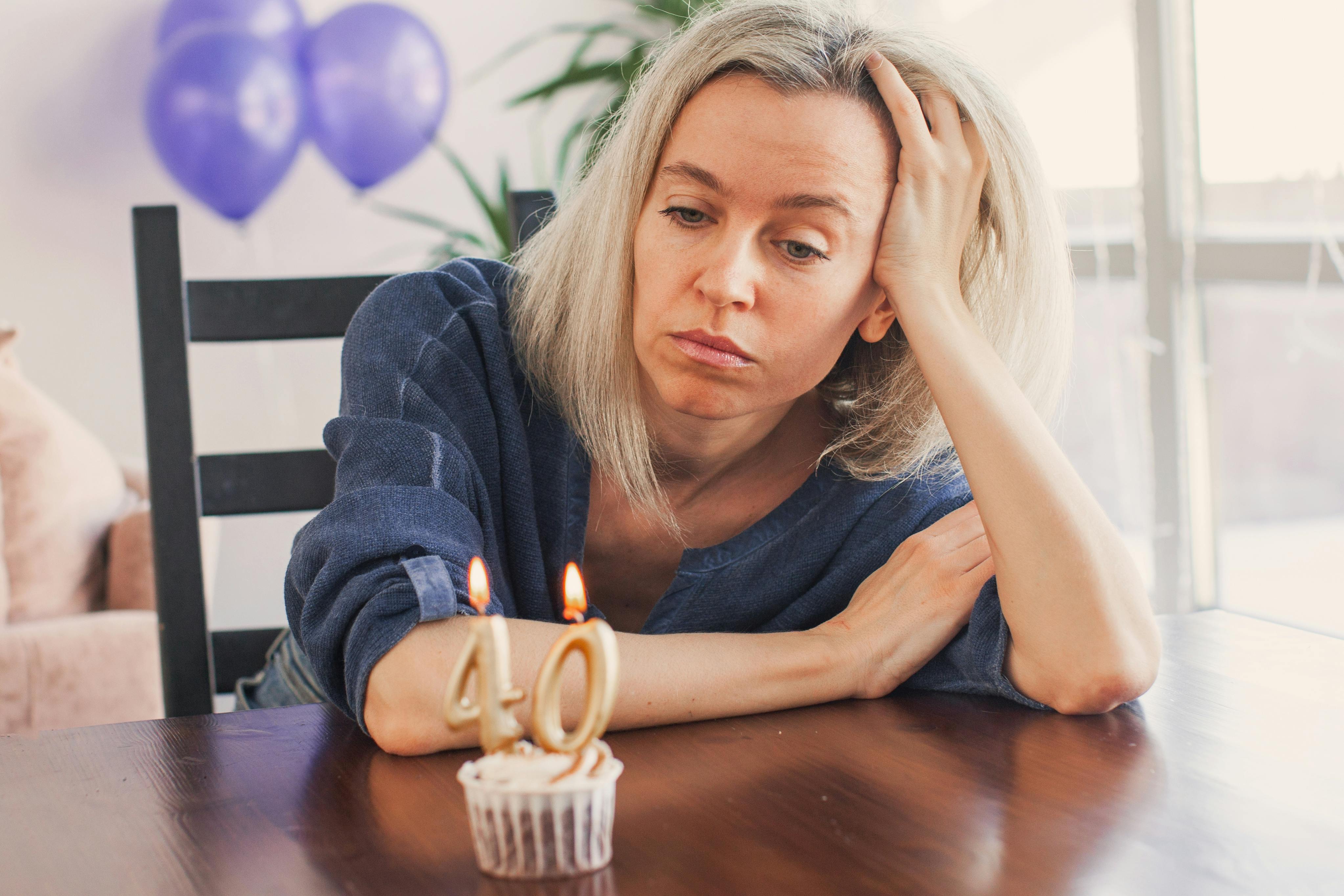 Kvinde sidder og ser trist på en enkelt lille muffin med et 40-års fødselsdagslys i.