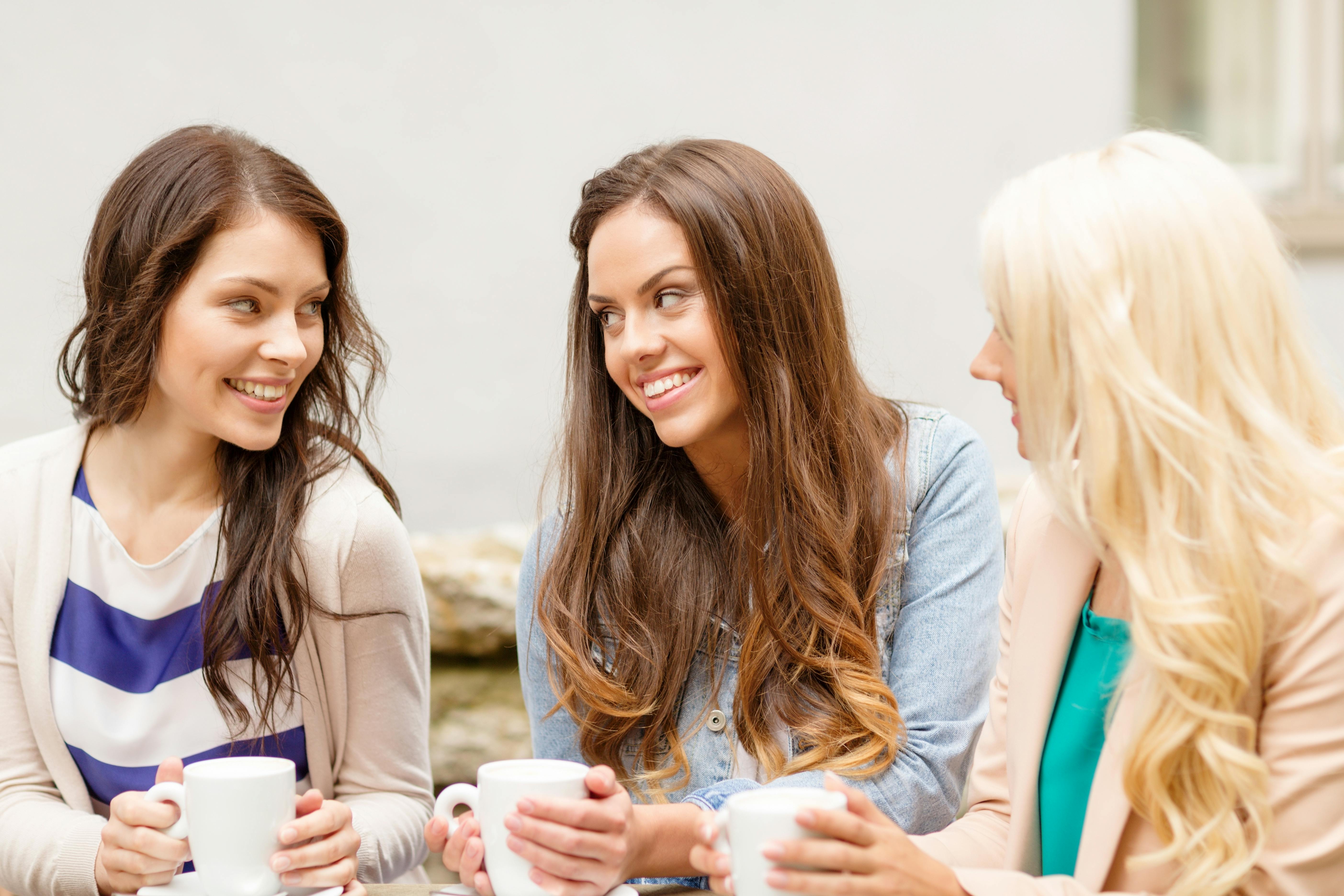 Tre unge kvinder sidder og taler sammen over en kop kaffe