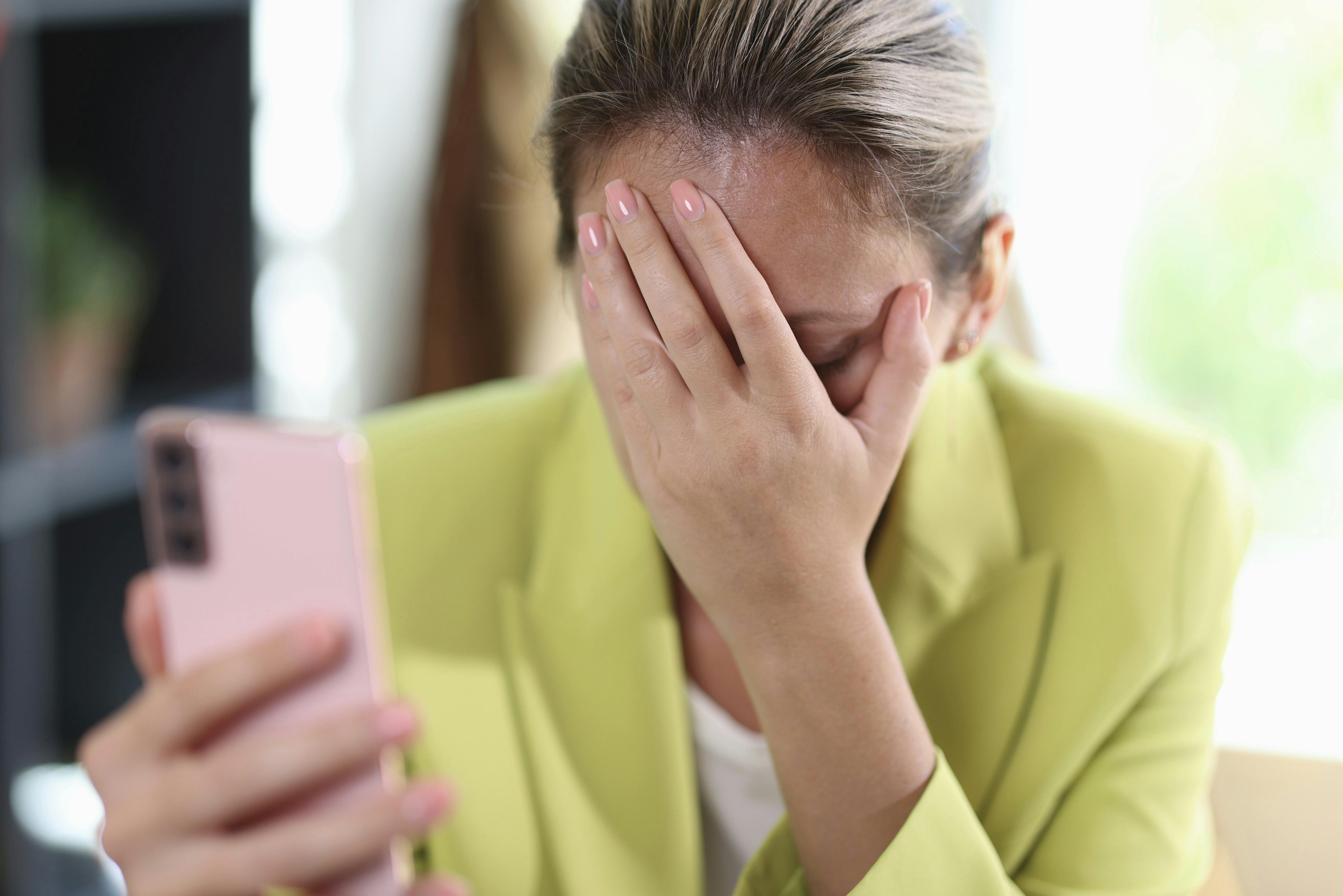 Close-up of frustrated depressed woman covering face with hand. Female holding smartphone and covering face with hand. Bad news or forgetfulness concept