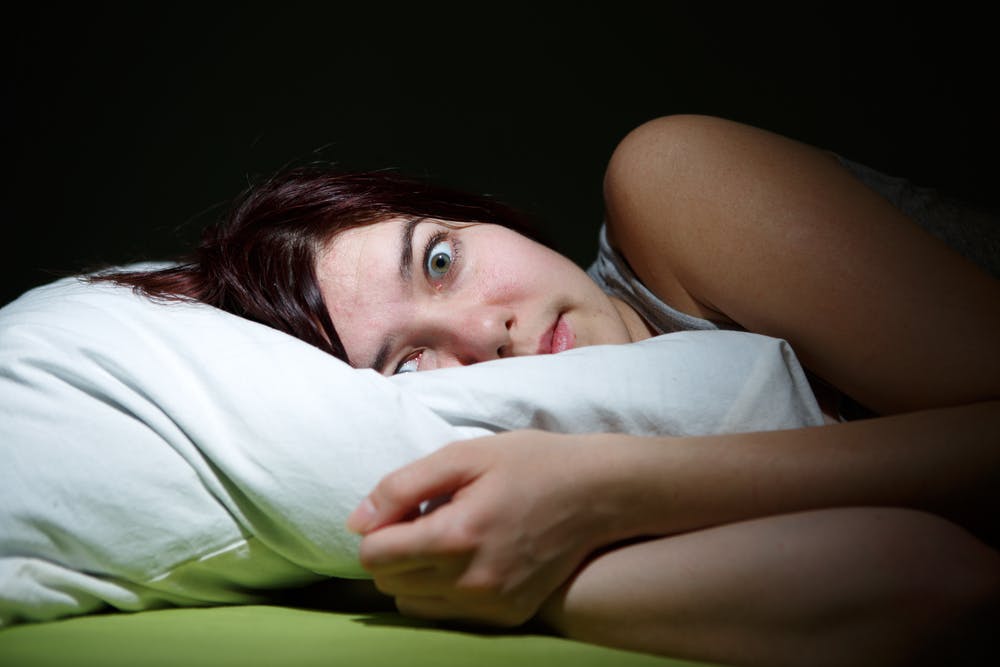 Ung kvinde ligger i sin seng og ser skrækslagen ud.