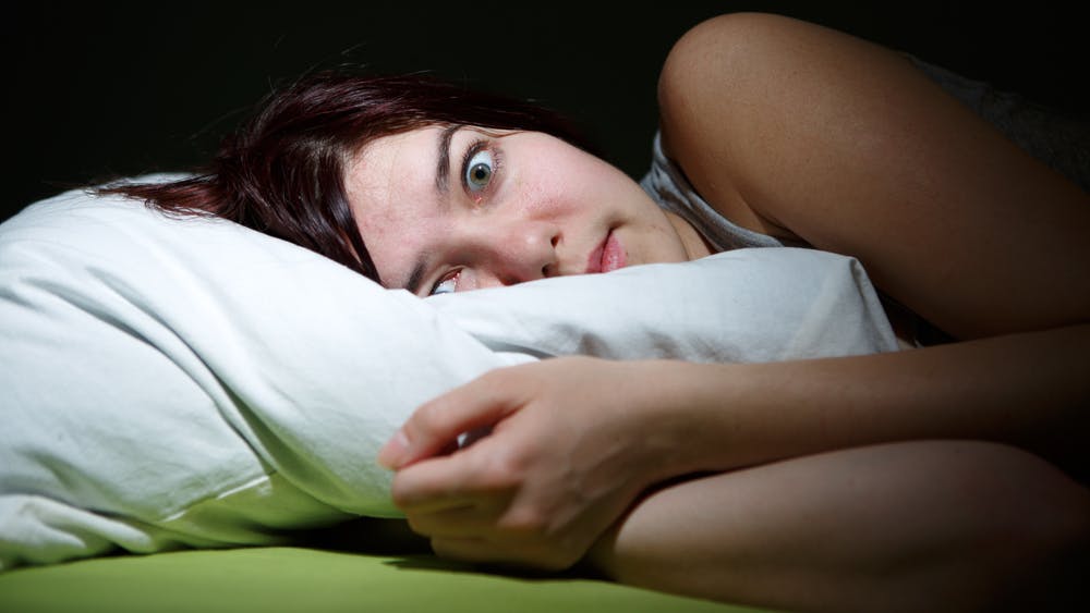 Ung kvinde ligger i sin seng og ser skrækslagen ud.