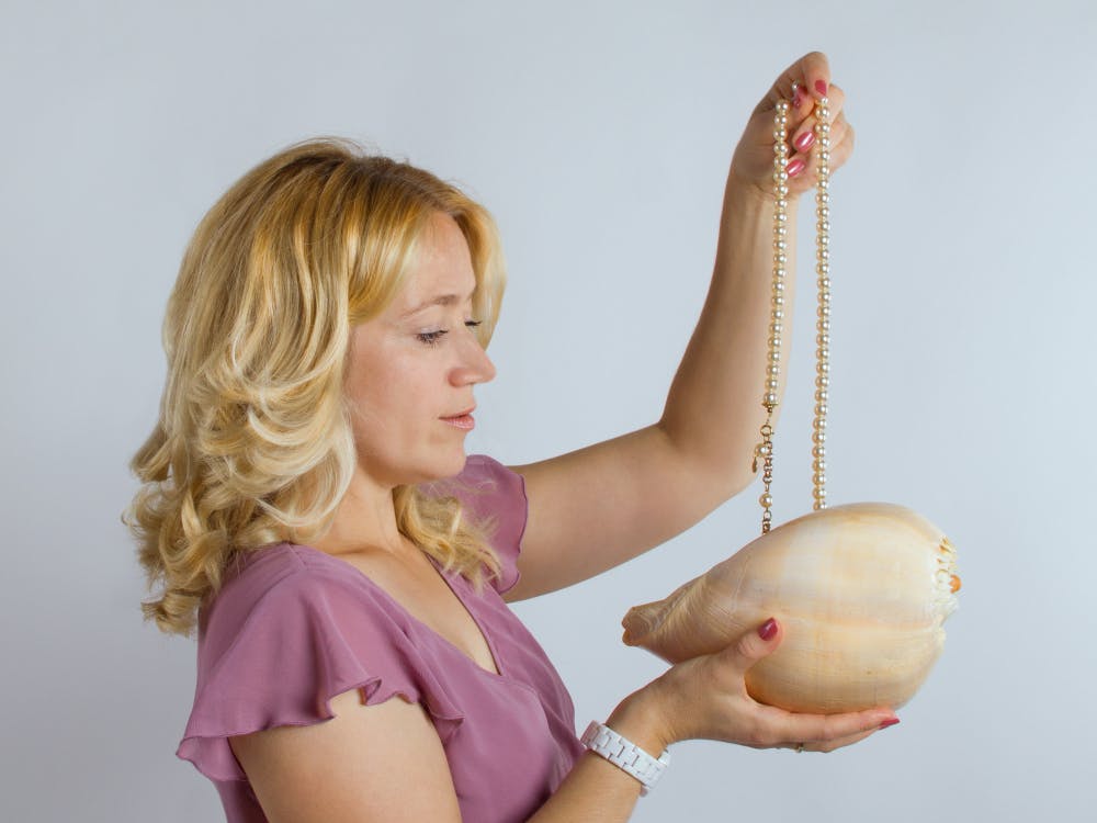 Kvinde tager en perlekæde op af en lille håndtaske.