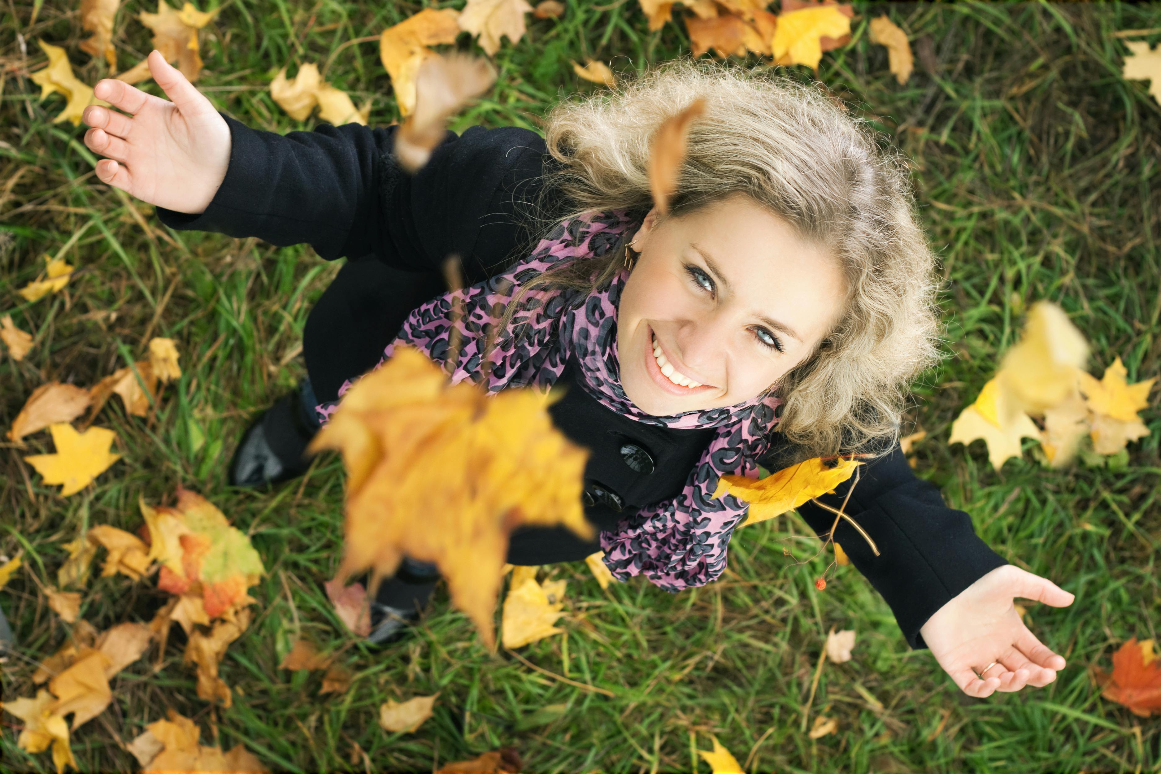 Ung pige ser smilende op mod faldende efterårsblade.