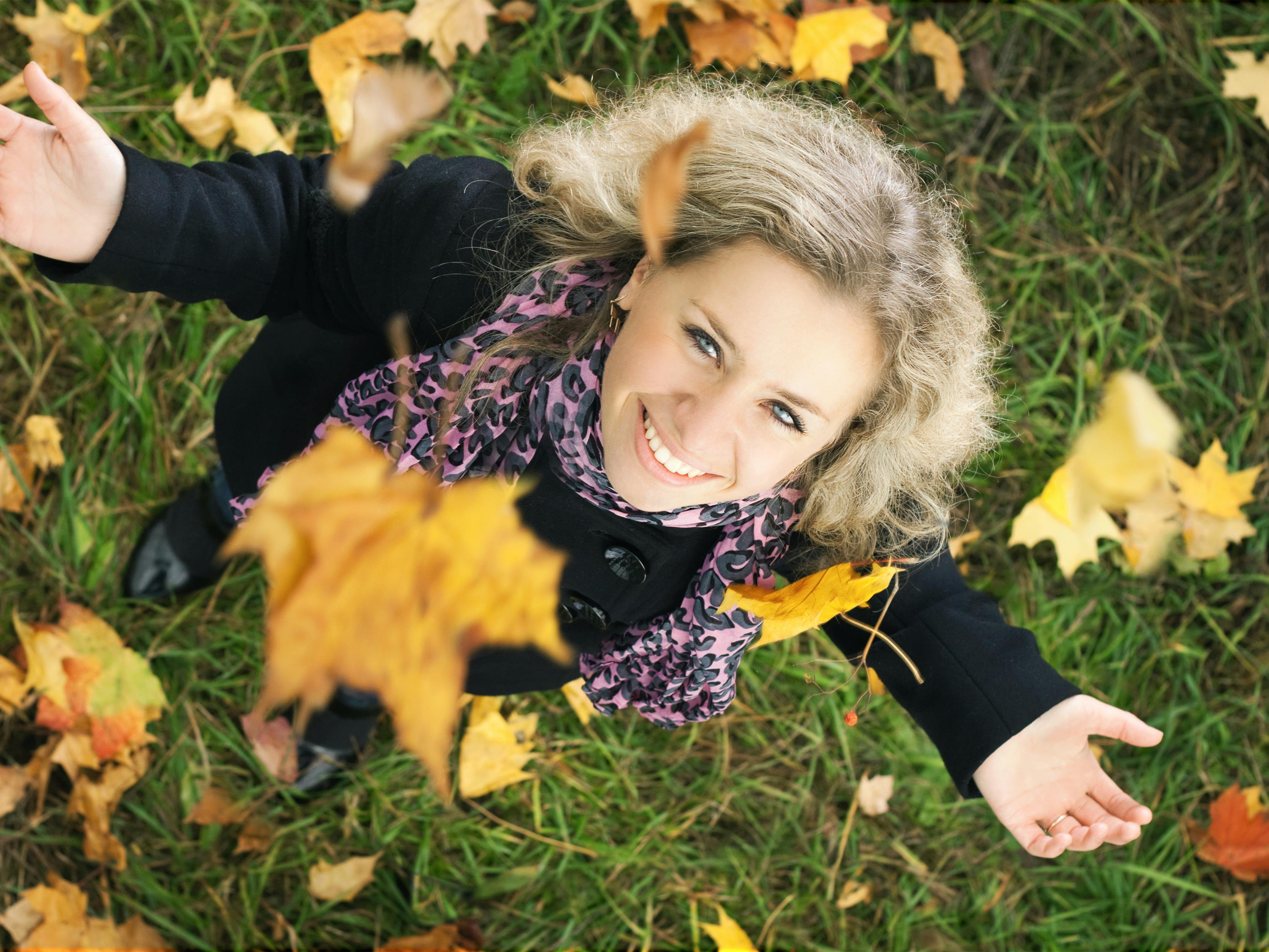 Ung pige ser smilende op med faldende efterårsblade.