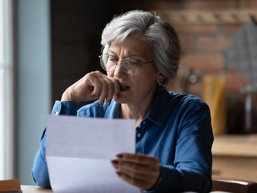 Ældre kvinde læser et brev med et bekymret udtryk.