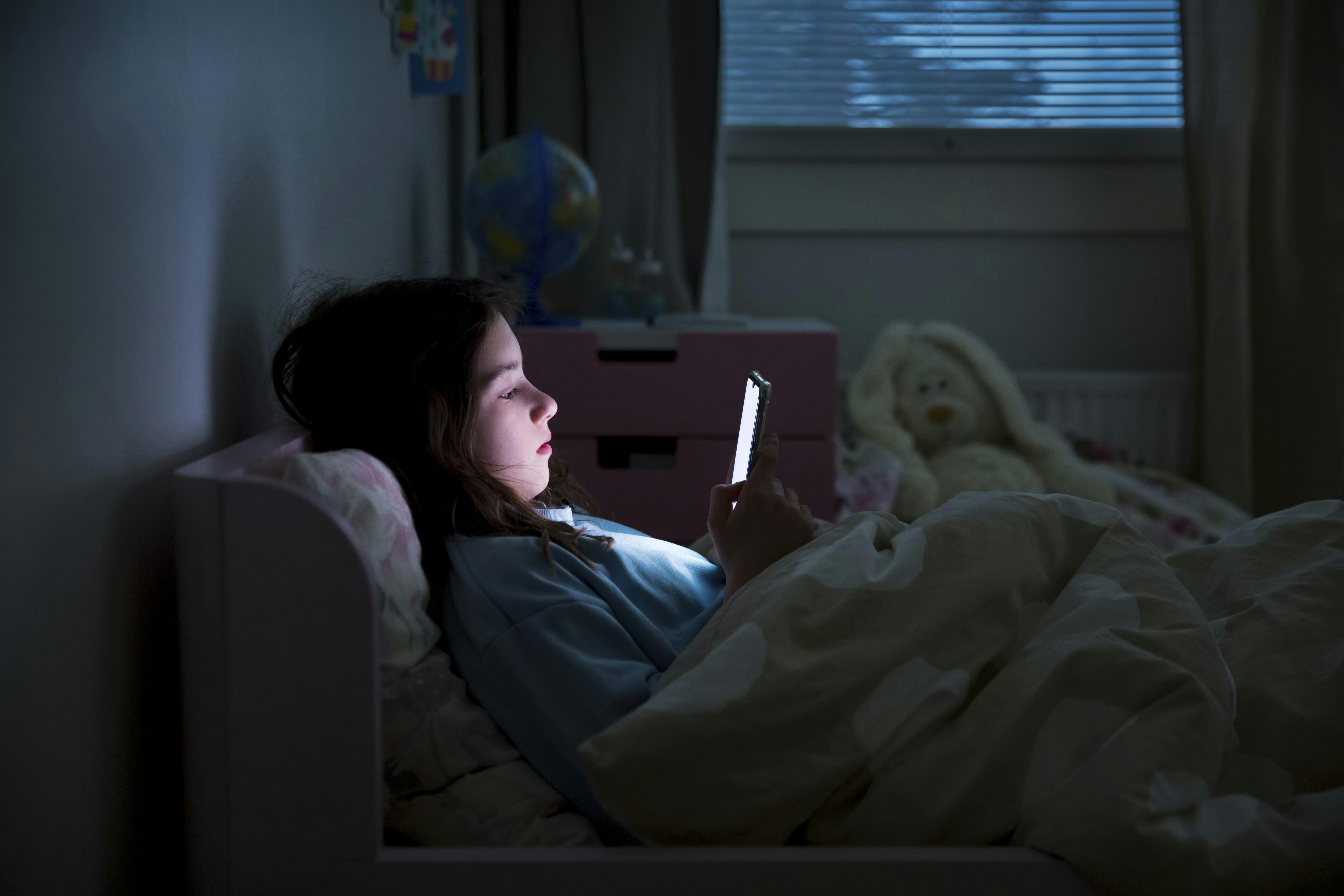 børns skærmforbrug, pige ligger i sengen med mobil