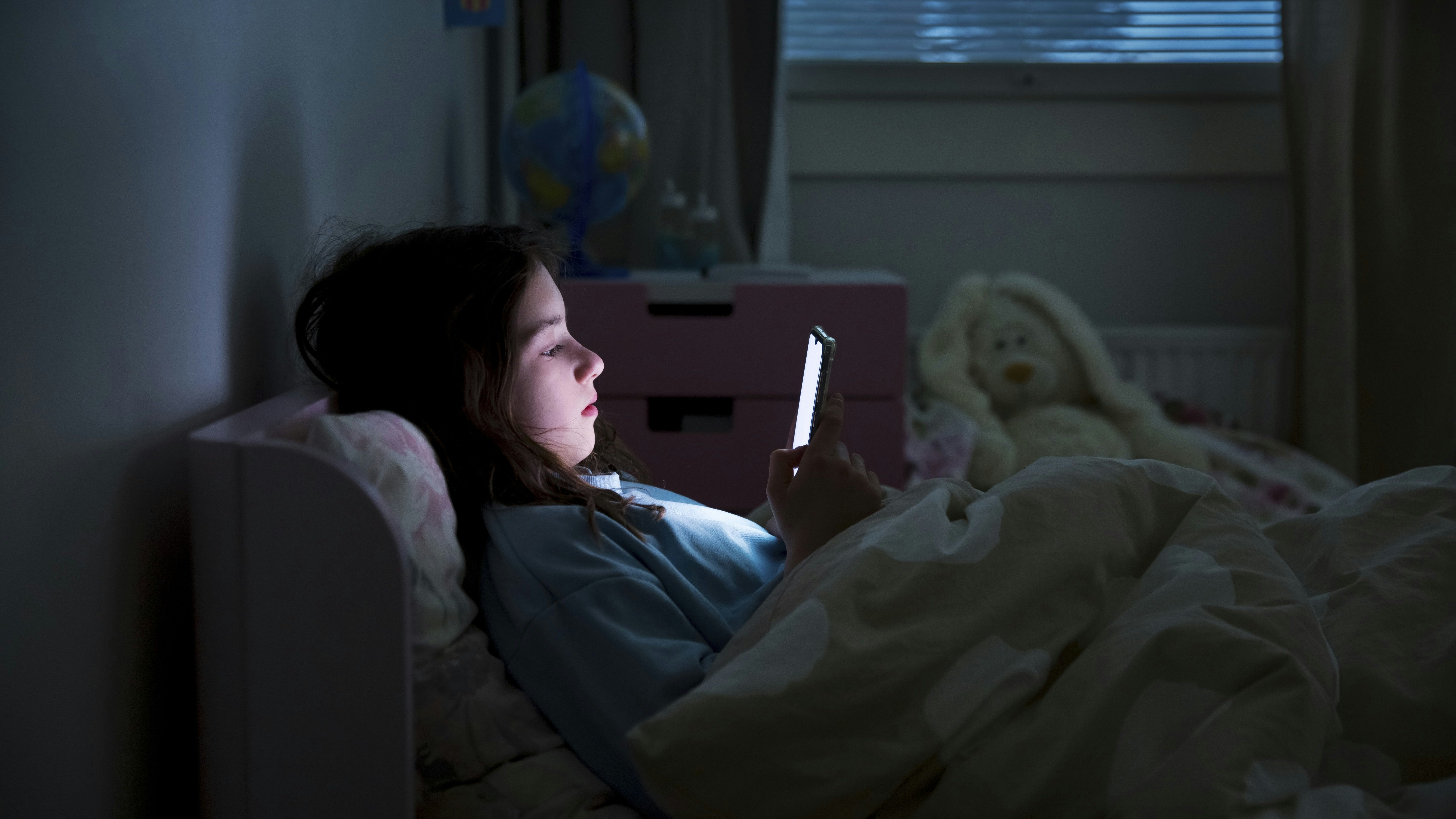 børns skærmforbrug, pige ligger i sengen med mobil