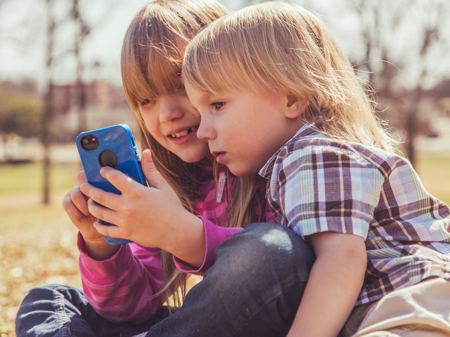 Søster og lillebror på 5 og 3 år ser begge på en mobiltelefon.