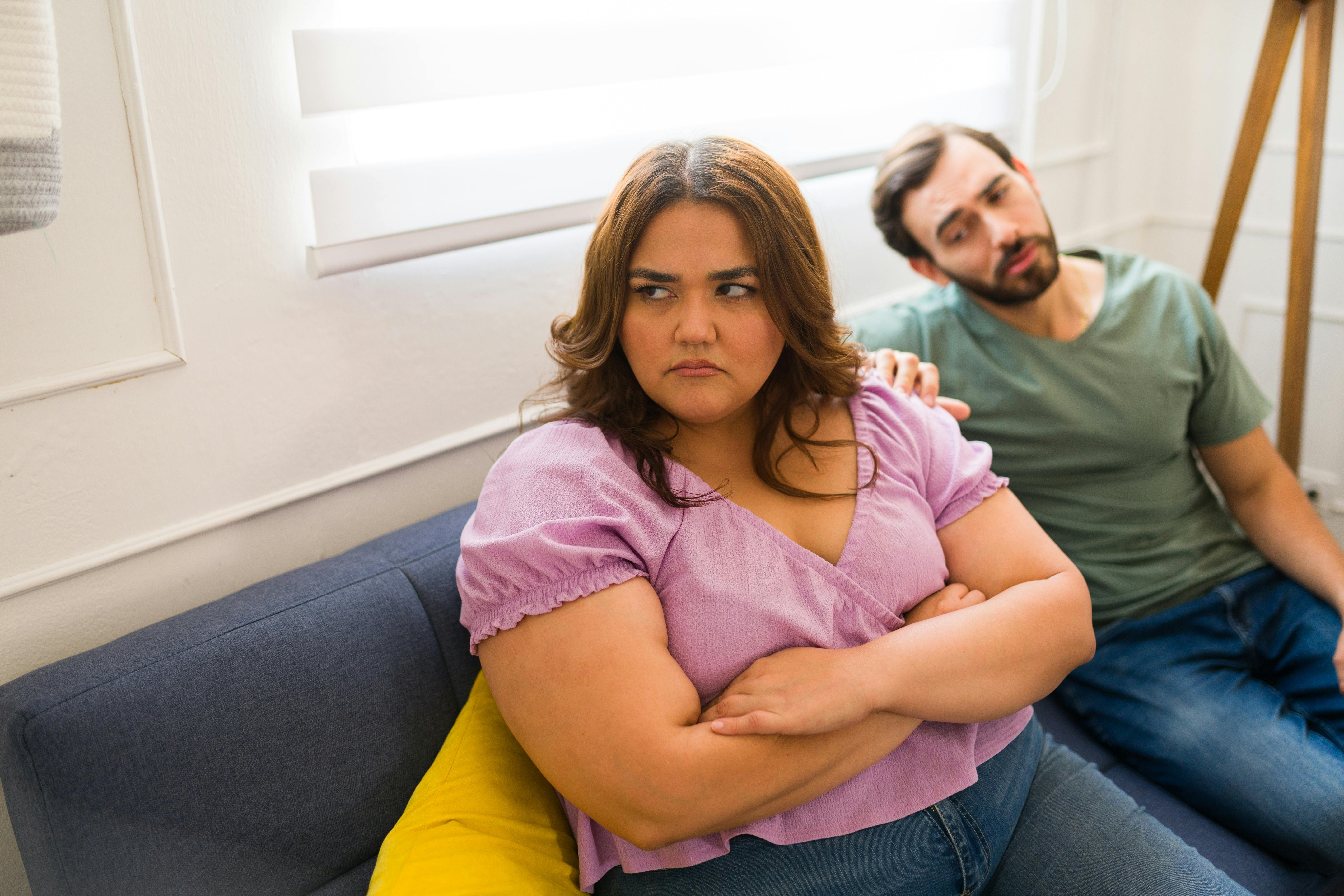 Overvægtig kvinde ser trist ud, mens hendes mand ser til i baggrunden.