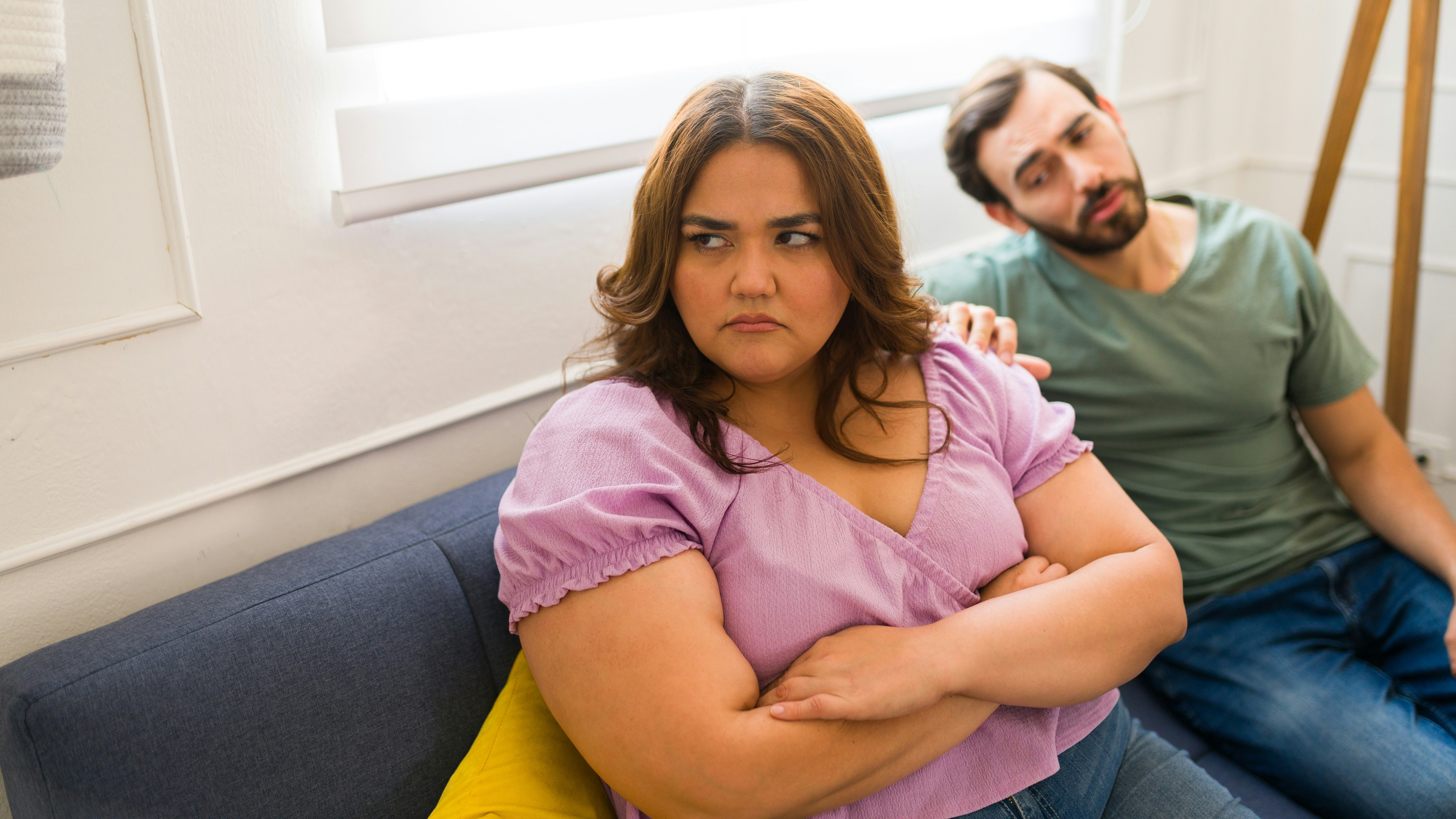 Overvægtig kvinde ser trist ud, mens hendes mand ser til i baggrunden.