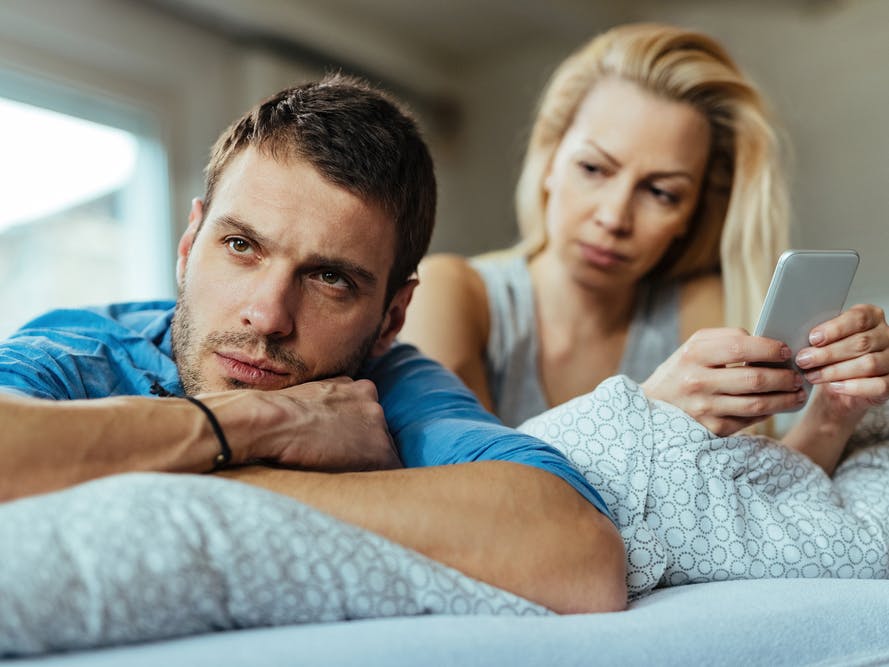Kvinde ligger i sengen og ser skeptisk på sin mand.