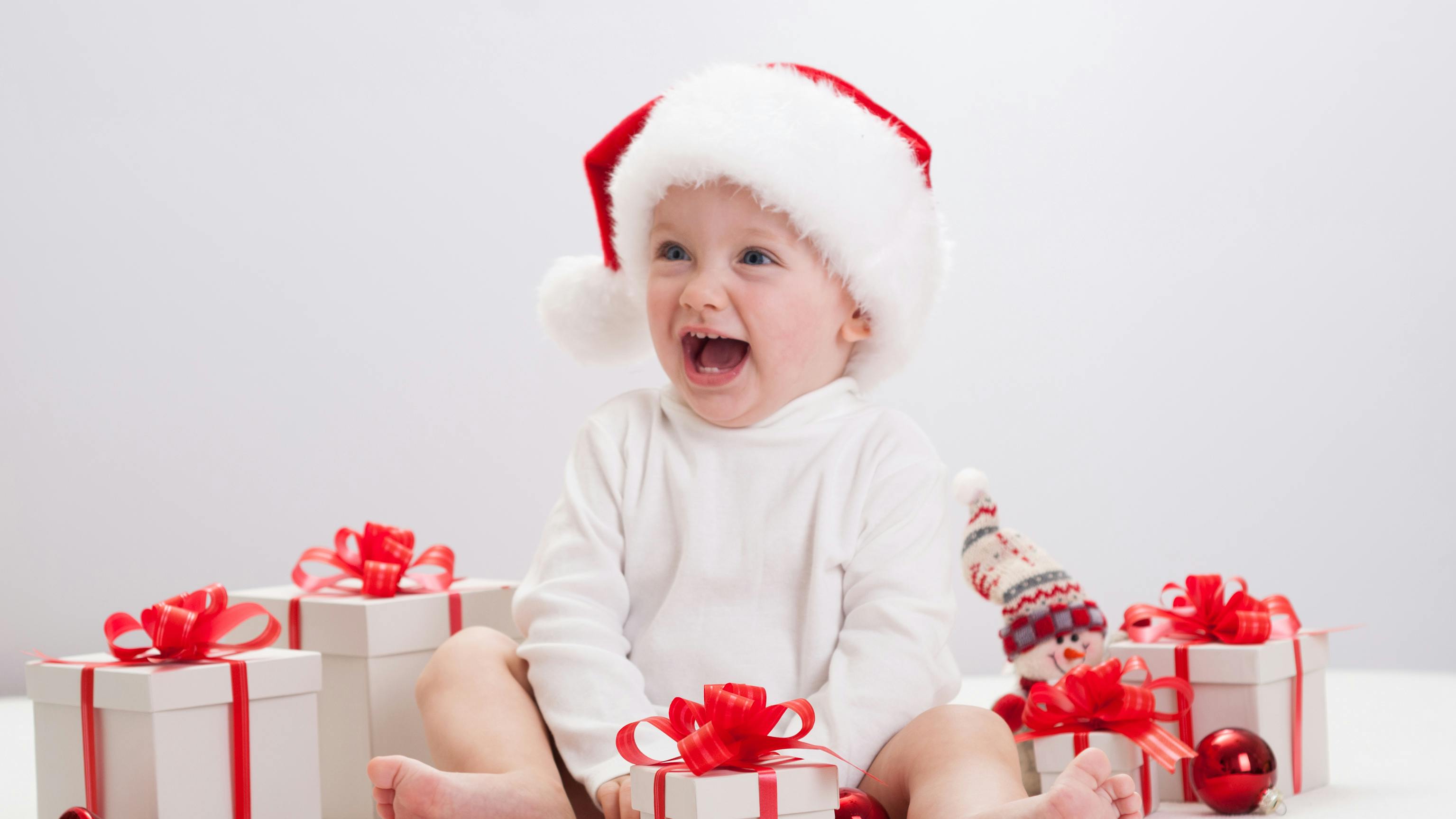 Lille pige med nissehue sidder med julegaver omkring sig.