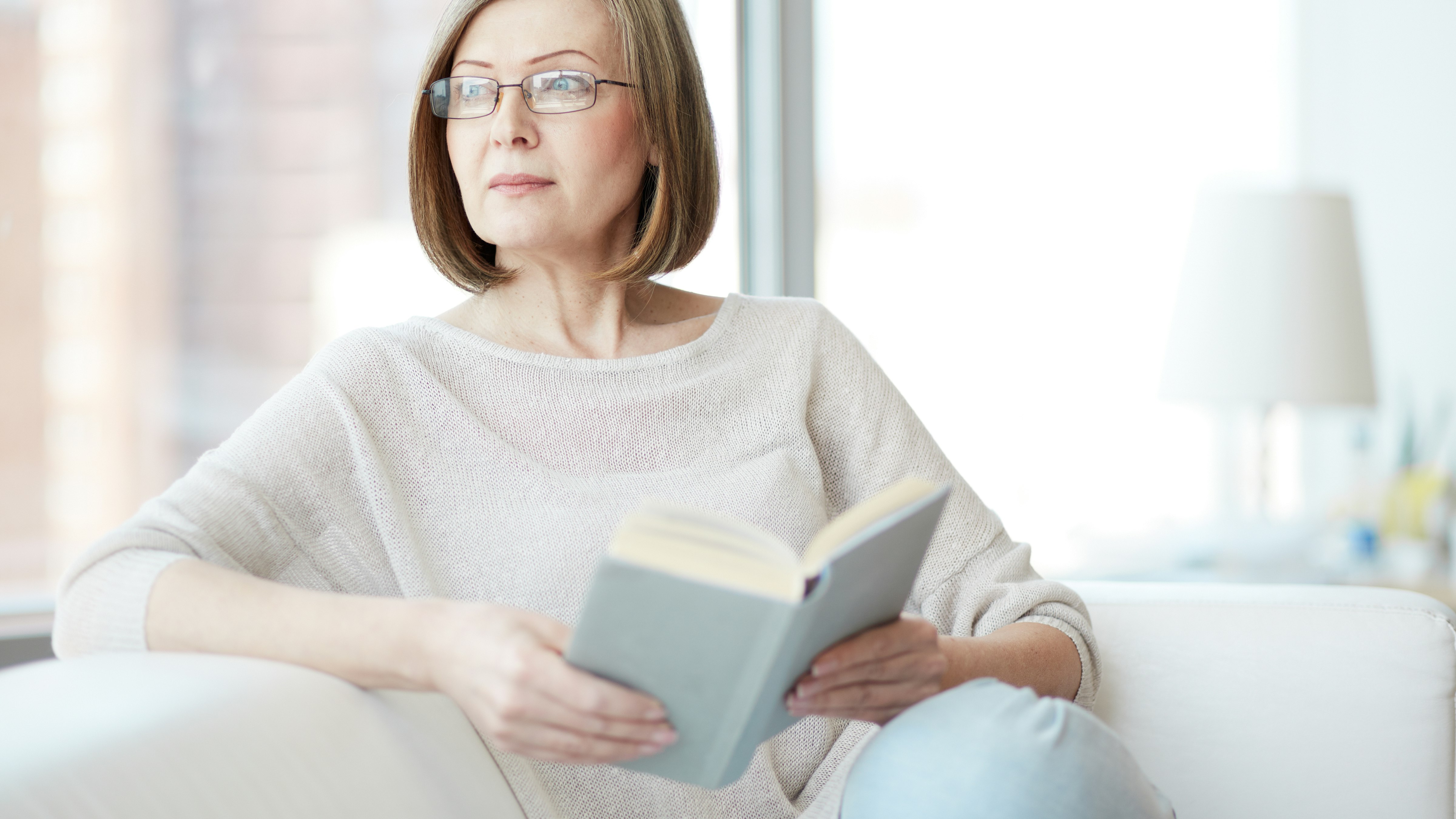 Kvinde sidder i en sofa og læser en bog
