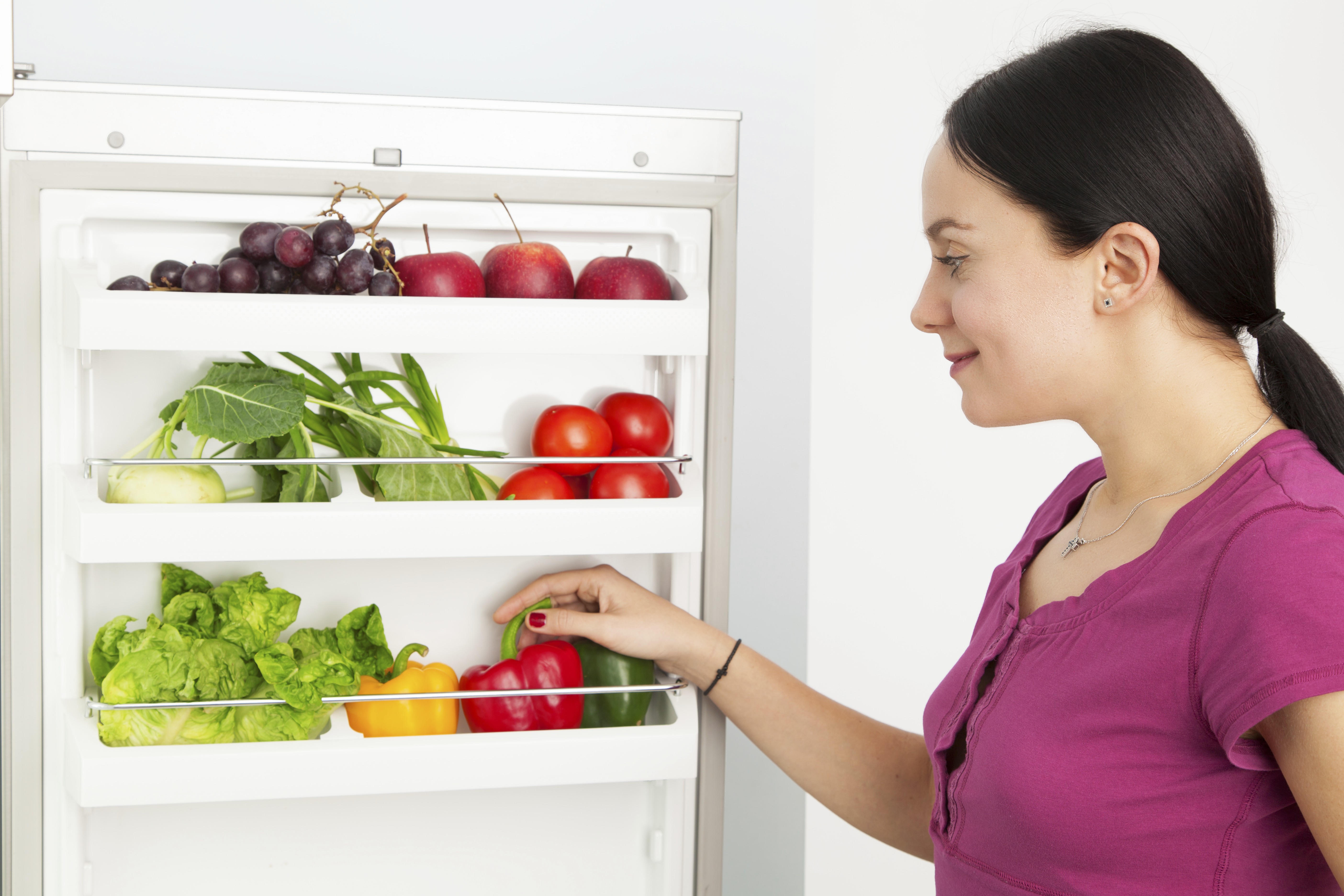 Kvinde kigger ind i køleskab fyldt med grøntsager