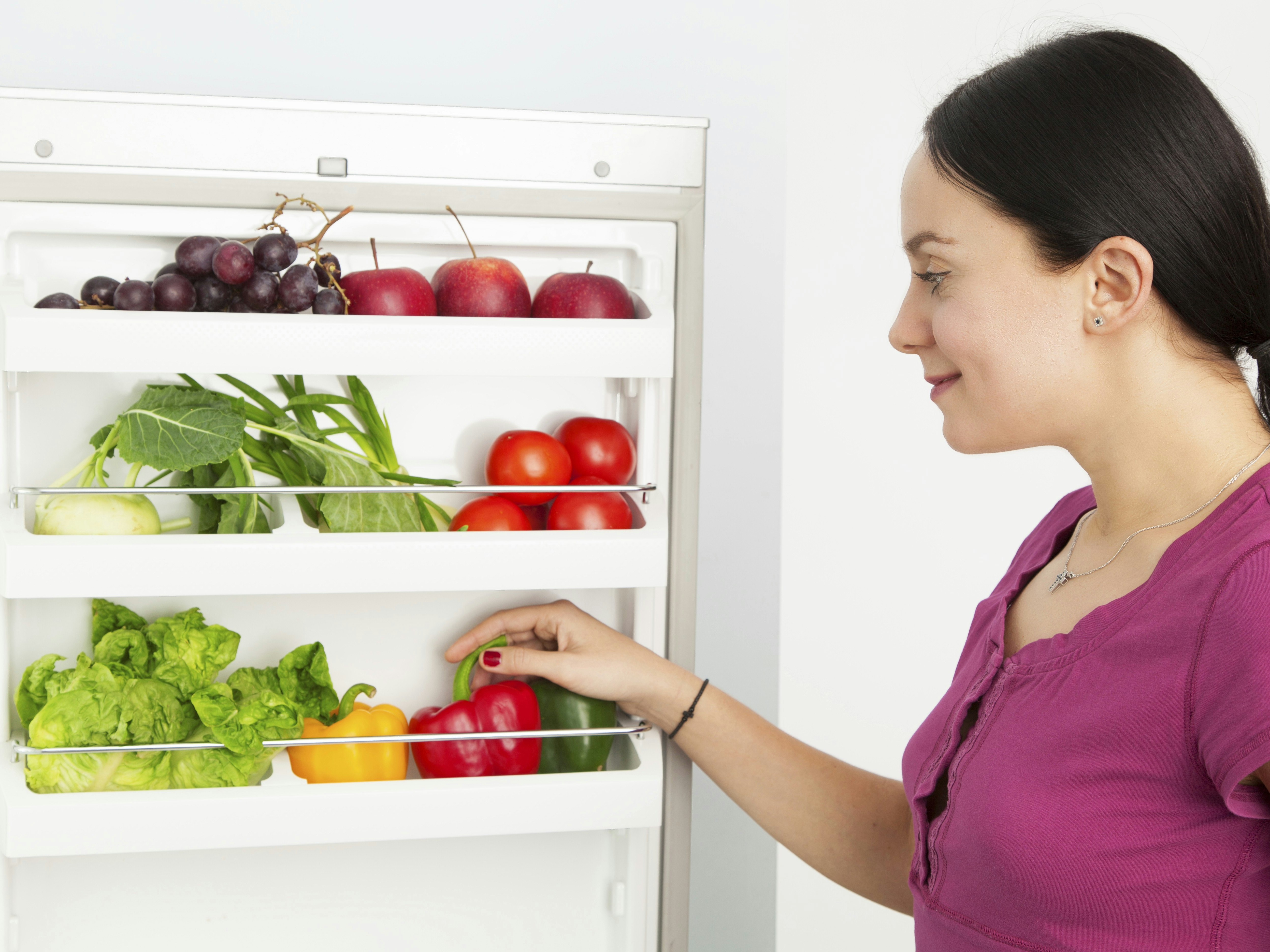 Kvinde kigger ind i køleskab fyldt med grøntsager