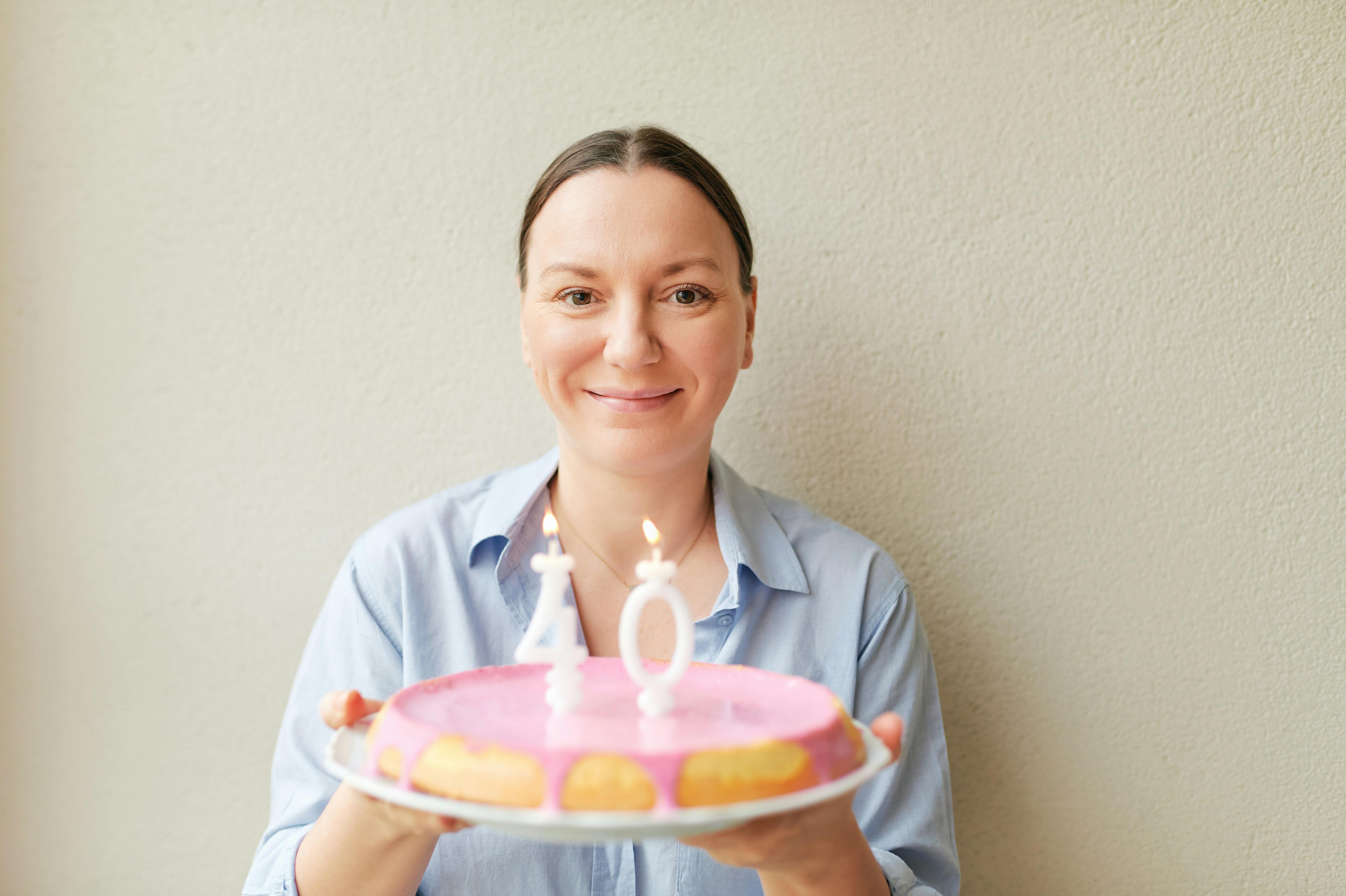 40-årig Kvinde holder en lagkage med fødselsdagslys frem for sig.