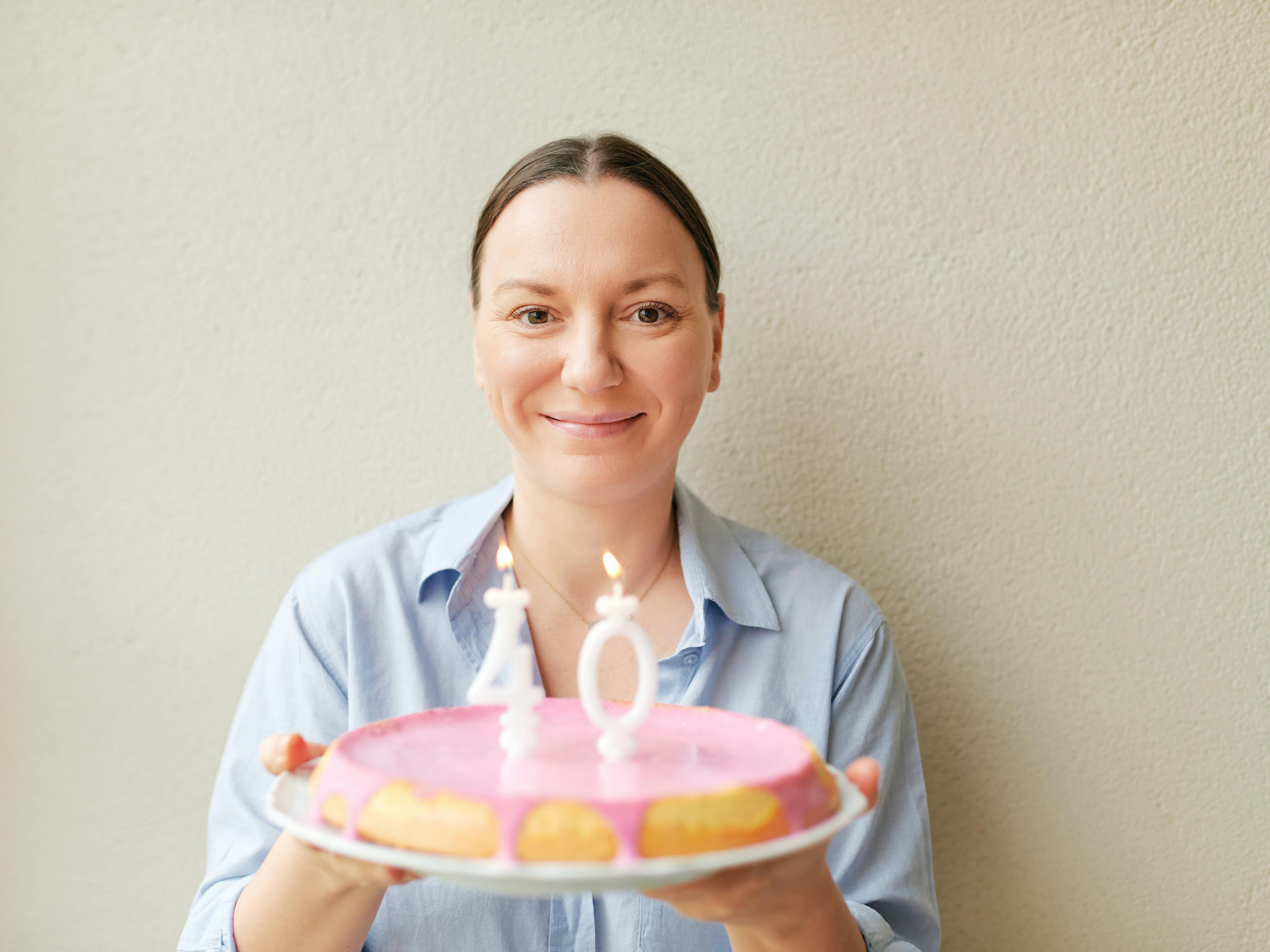 40-årig Kvinde holder en lagkage med fødselsdagslys frem for sig.