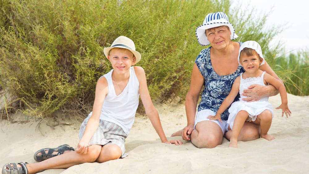 Bedstemor sidder på stranden og hygger sig med sine to børnebørn.