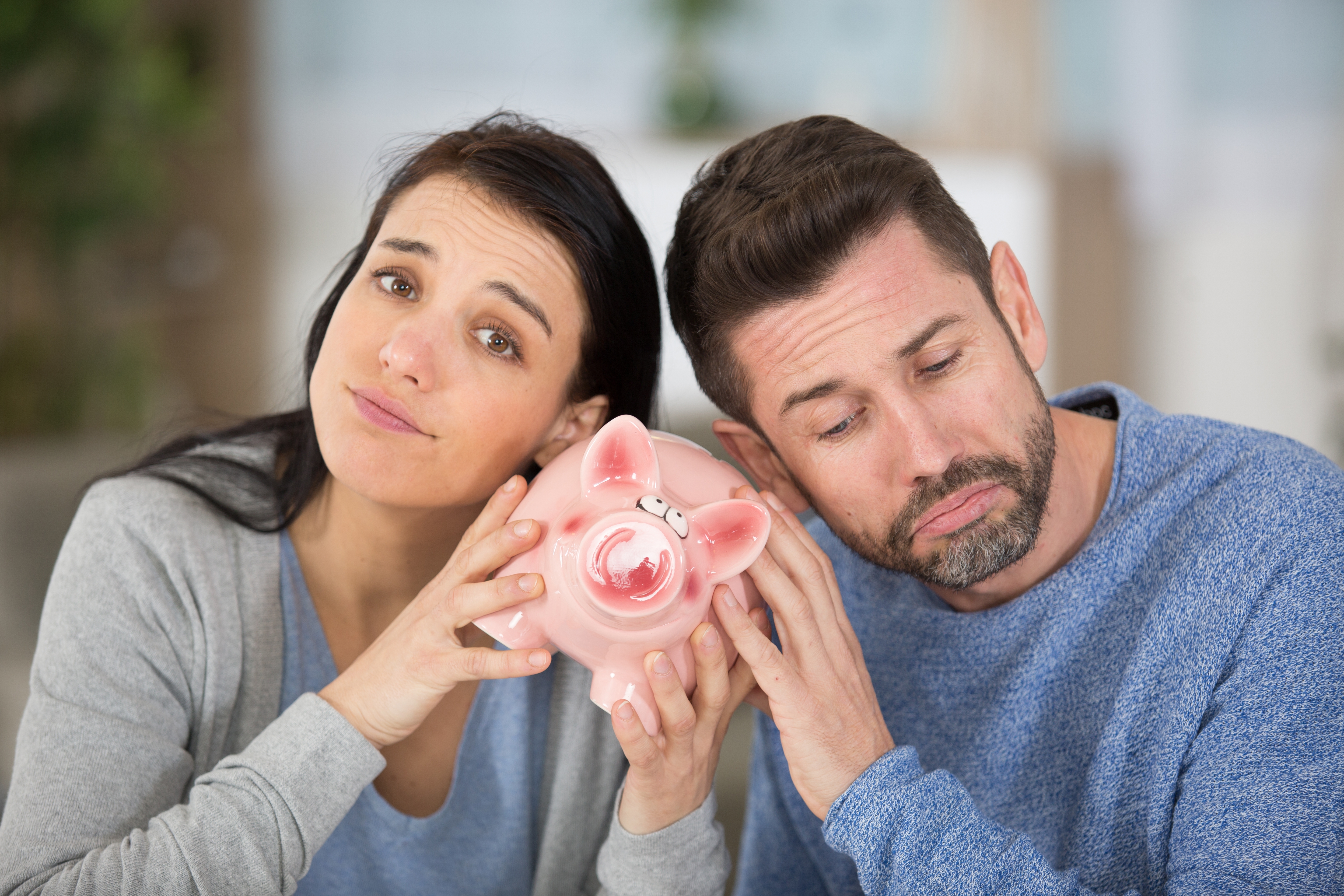 Mand og kvinde holder en sparegris imellem sig, mens de ser slukørede ud.