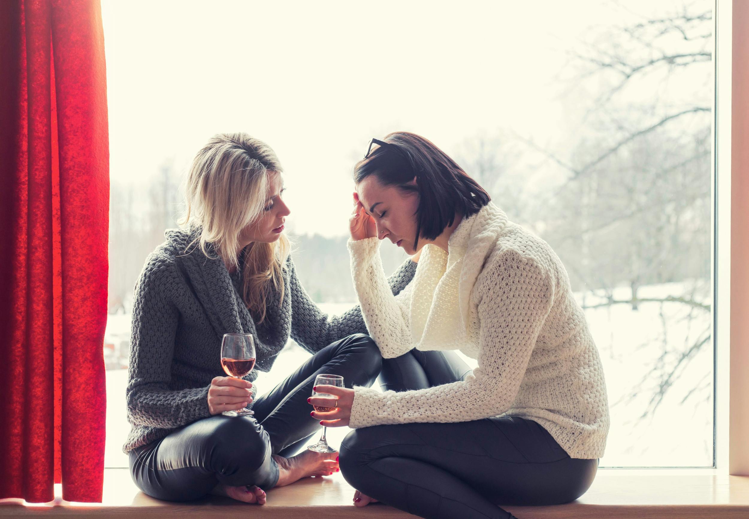 Kvinde trøster sin sørgende veninde. Begge sidder med et glas vin.