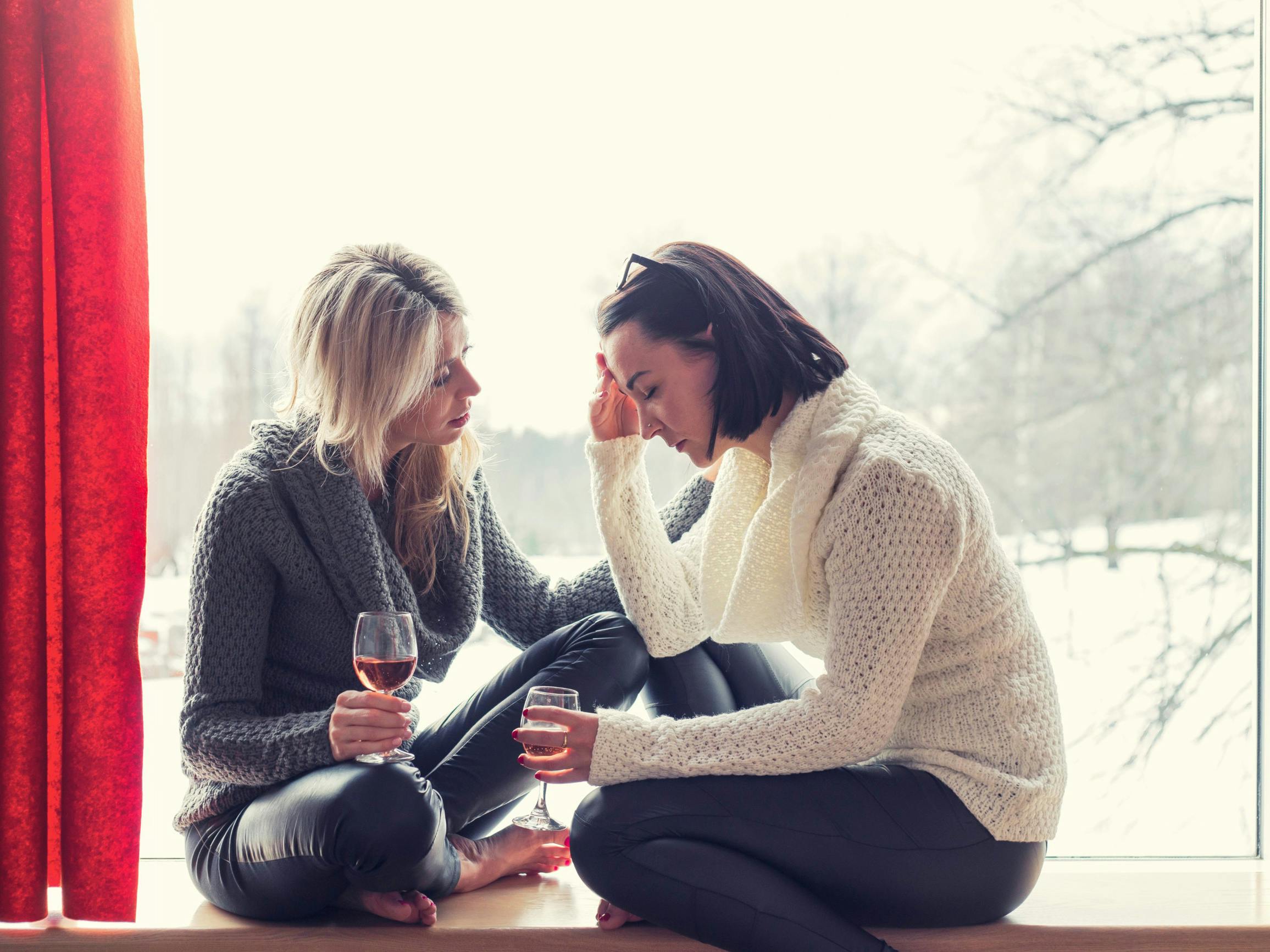 Kvinde trøster sin sørgende veninde. De sidder begge med et glas vin.
