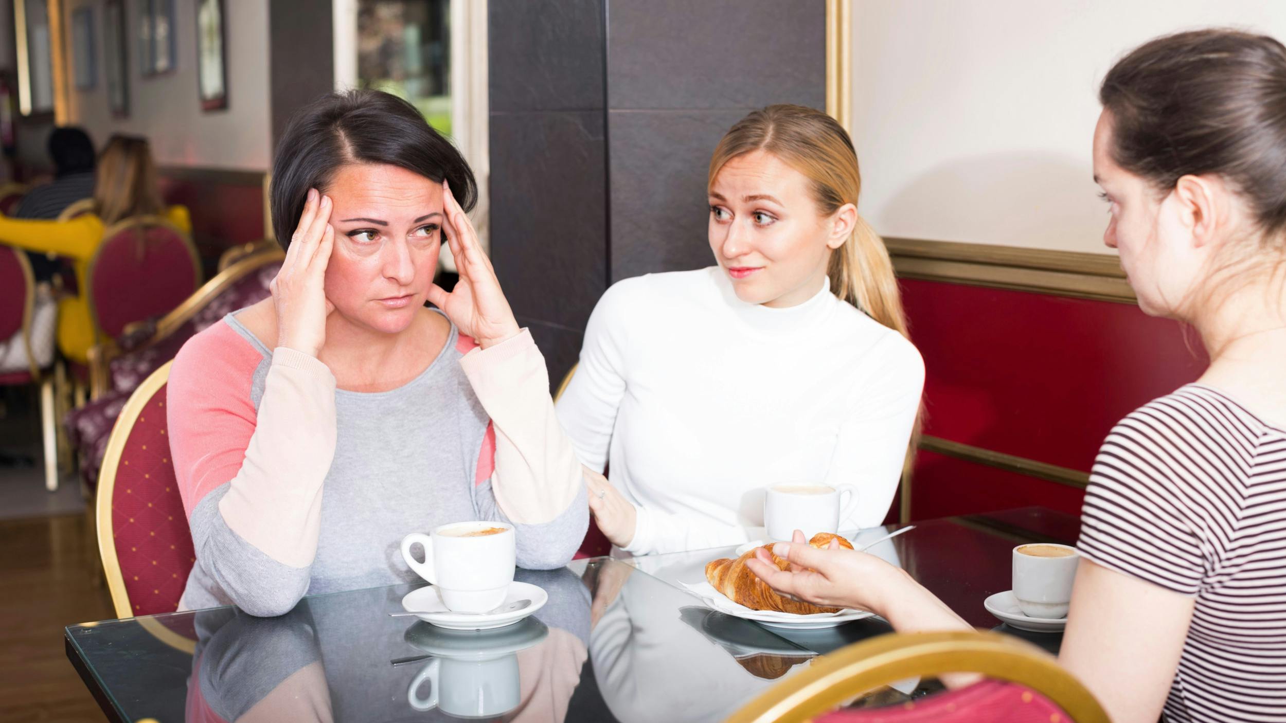 Tre kvinder drikker kaffe på en café, og den ene ser trist ud.