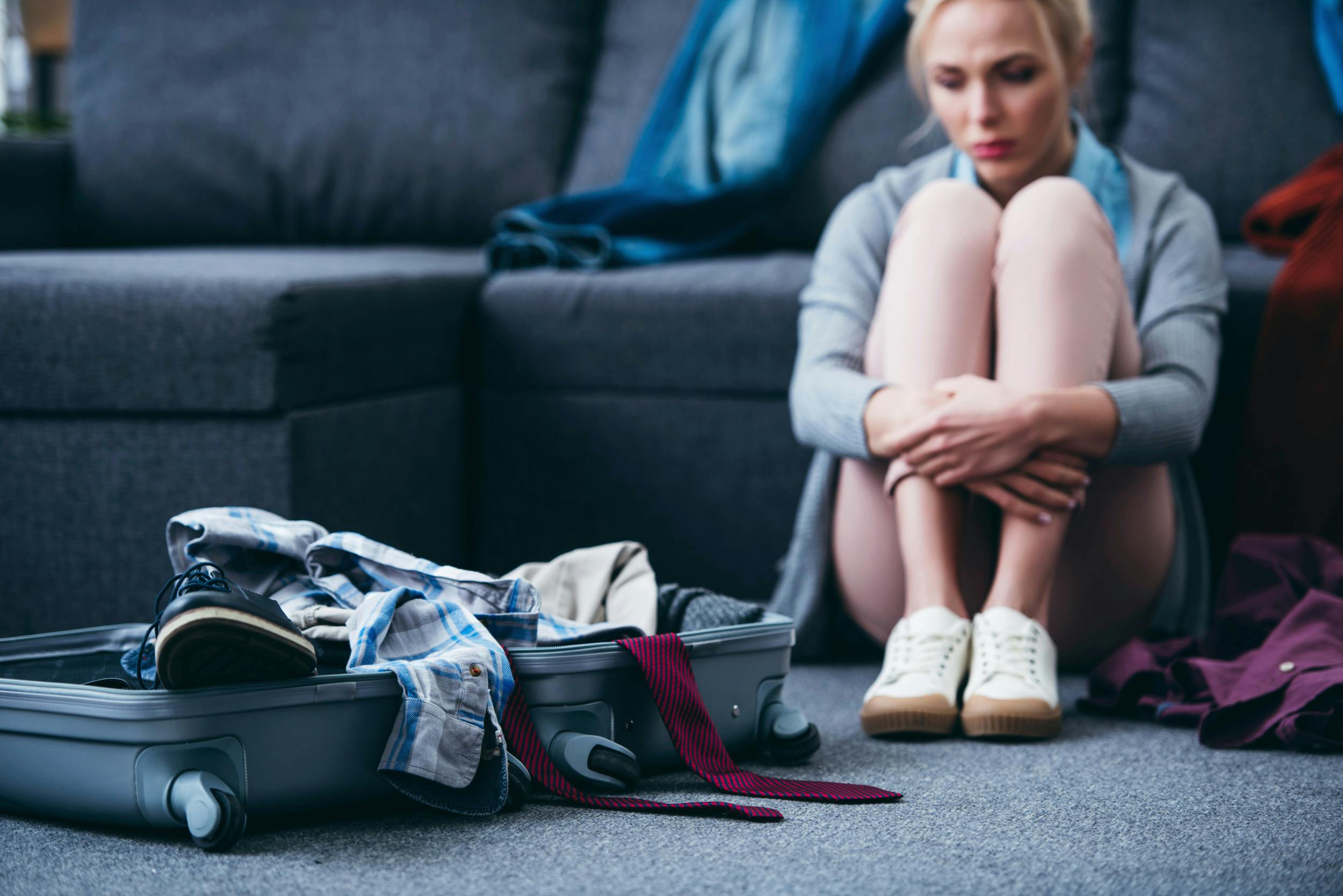 Ung kvinde sidder på gulvet ved siden af en kuffert fyldt med tøj