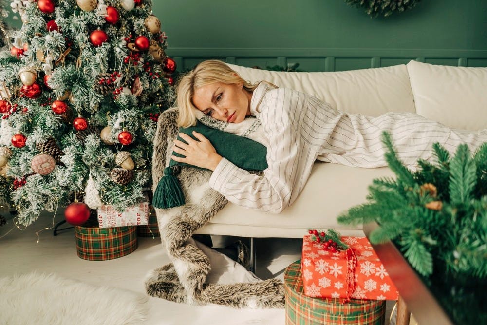 Træt, midaldrende kvinde ligger på sin sofa i sin julepyntede stue.