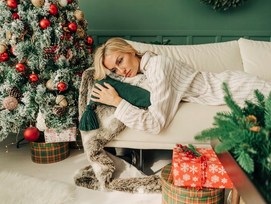 Træt, midaldrende kvinde ligger på sin sofa i sin julepyntede stue.