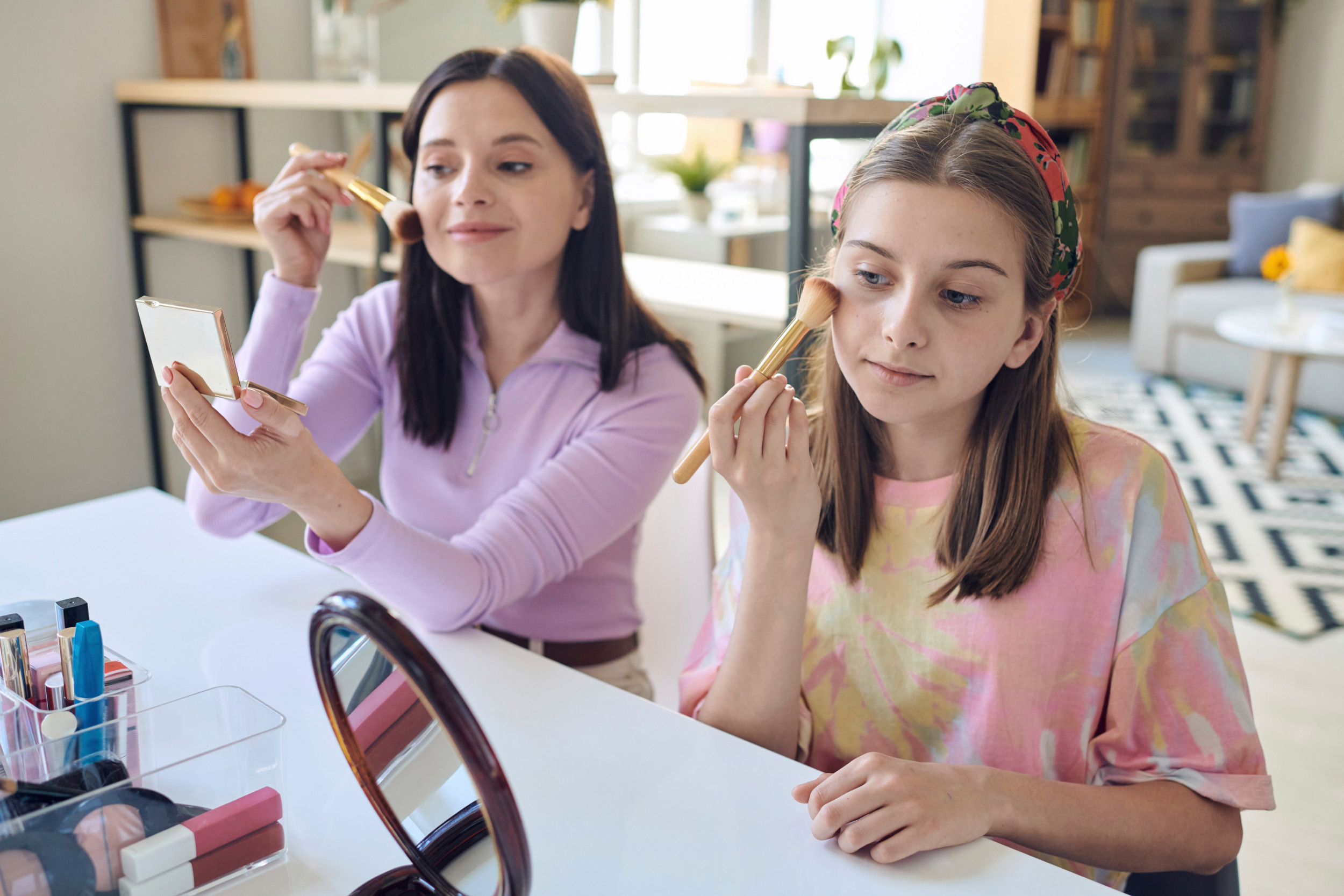 Mor og datter sidder side om side og lægger makeup