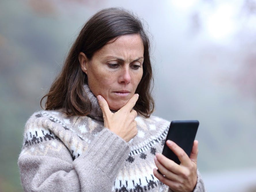 Midaldrende kvinde ser bekymret på sin mobil