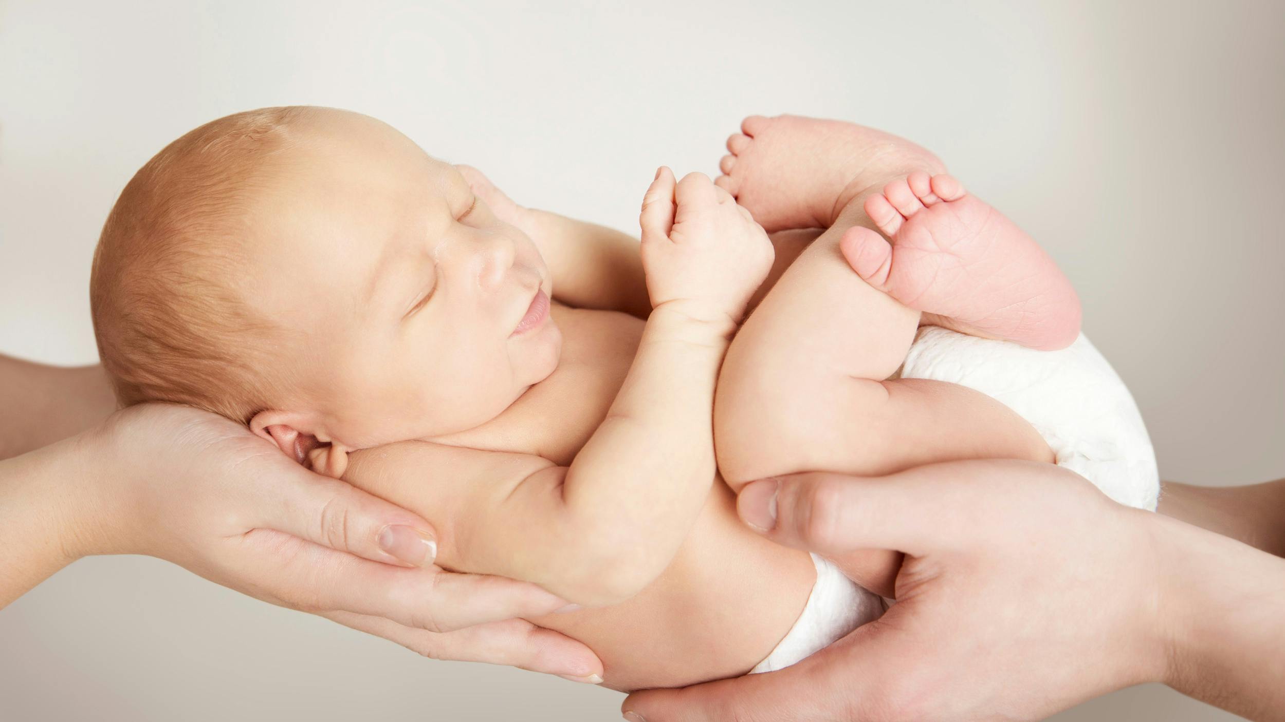 En nyfødt baby bliver holdt frem i hænderne på mor og far