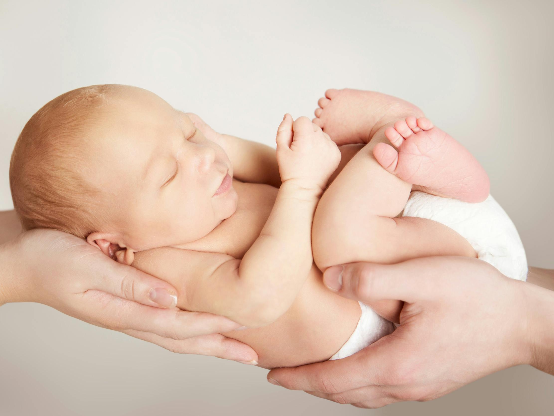 En nyfødt bliver holdt frem i hænderne på mor og far