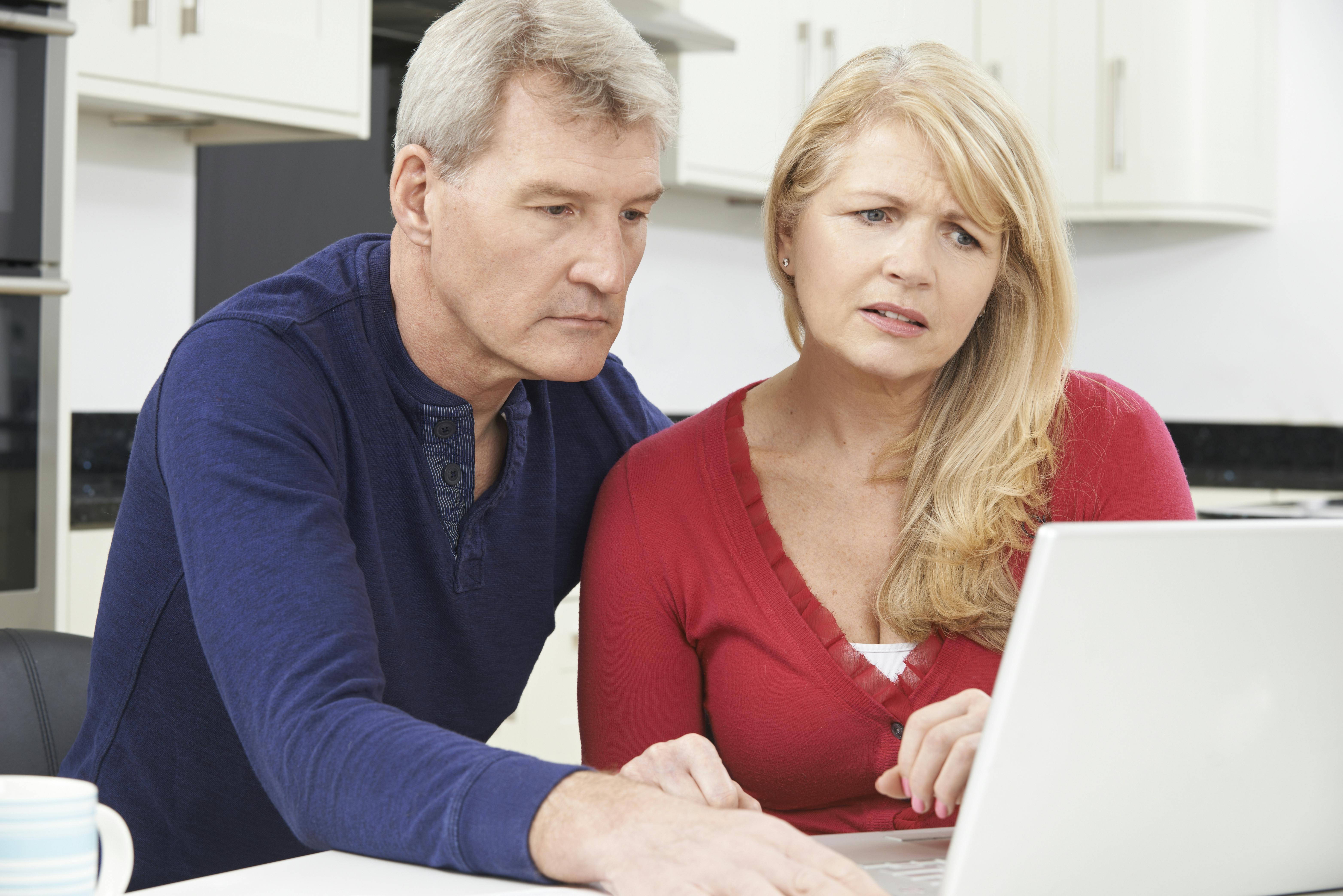 Bekymret midaldrende par sidder sammen ved deres bærbare computer.