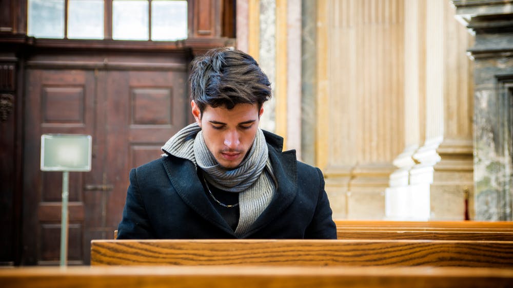 Ung mand sidder på en bænk i en kirke