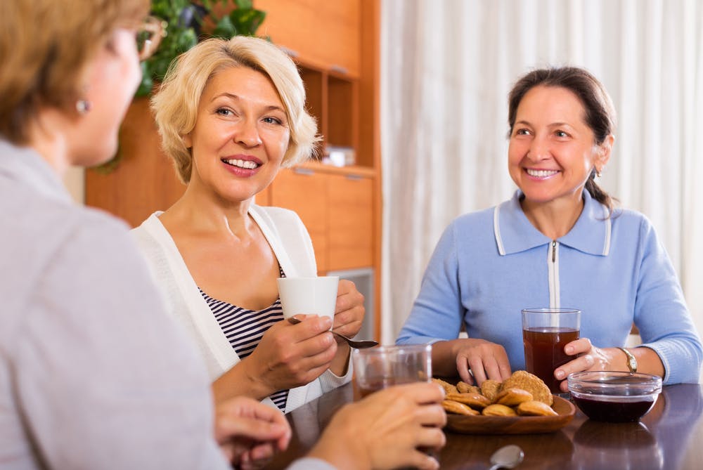 Tre kvinder sidder og taler sammen over en kop kaffe og småkager