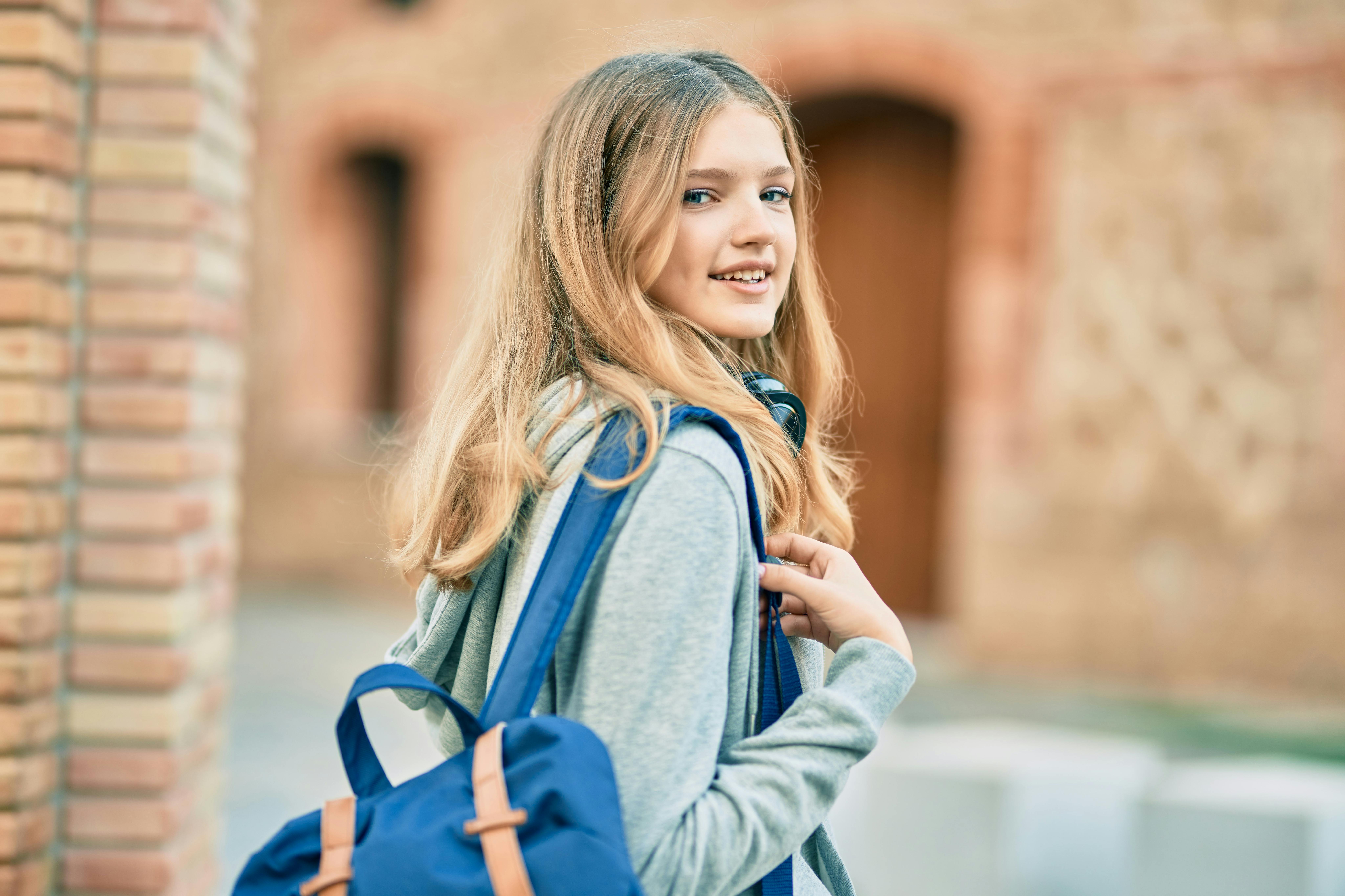 Teenagepige med skoletaske på ryggen går ind i skolegård.