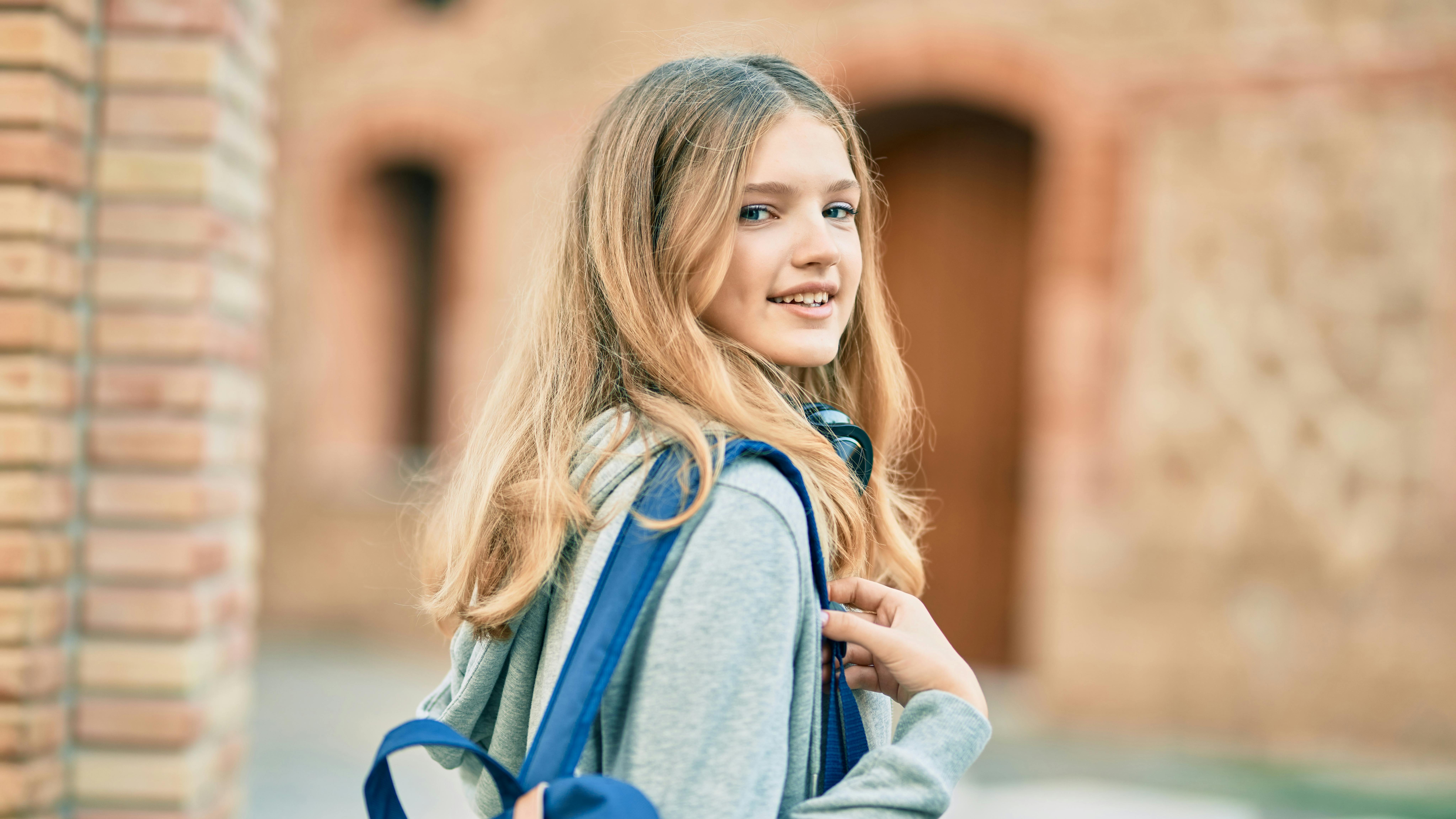 Teenagepige med skoletaske på ryggen går ind i skolegård.