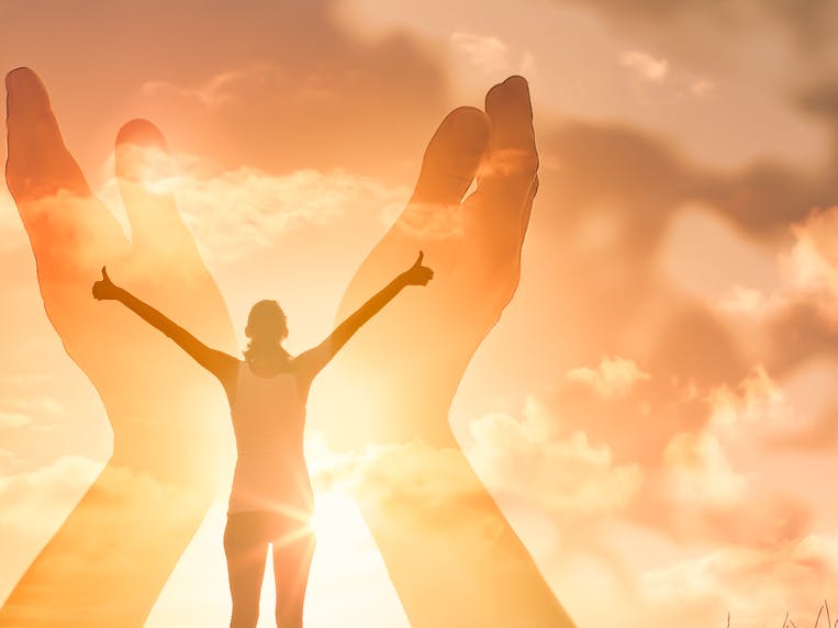 Kvinde står i et gult lys og rækker hænderne op i en skyet himmel. Hun er omgivet af to andre hænder
