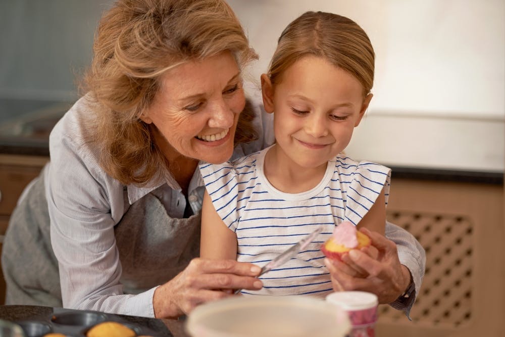 Mormor og barnebarn er ved at smøre smørcreme på en muffin