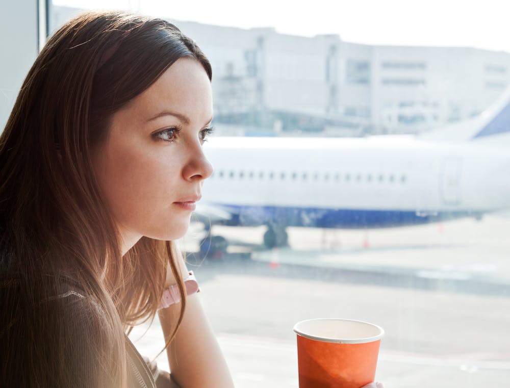 Ung kvinde i en lufthavn ser ud på et fly med et eftertænksomt udtryk