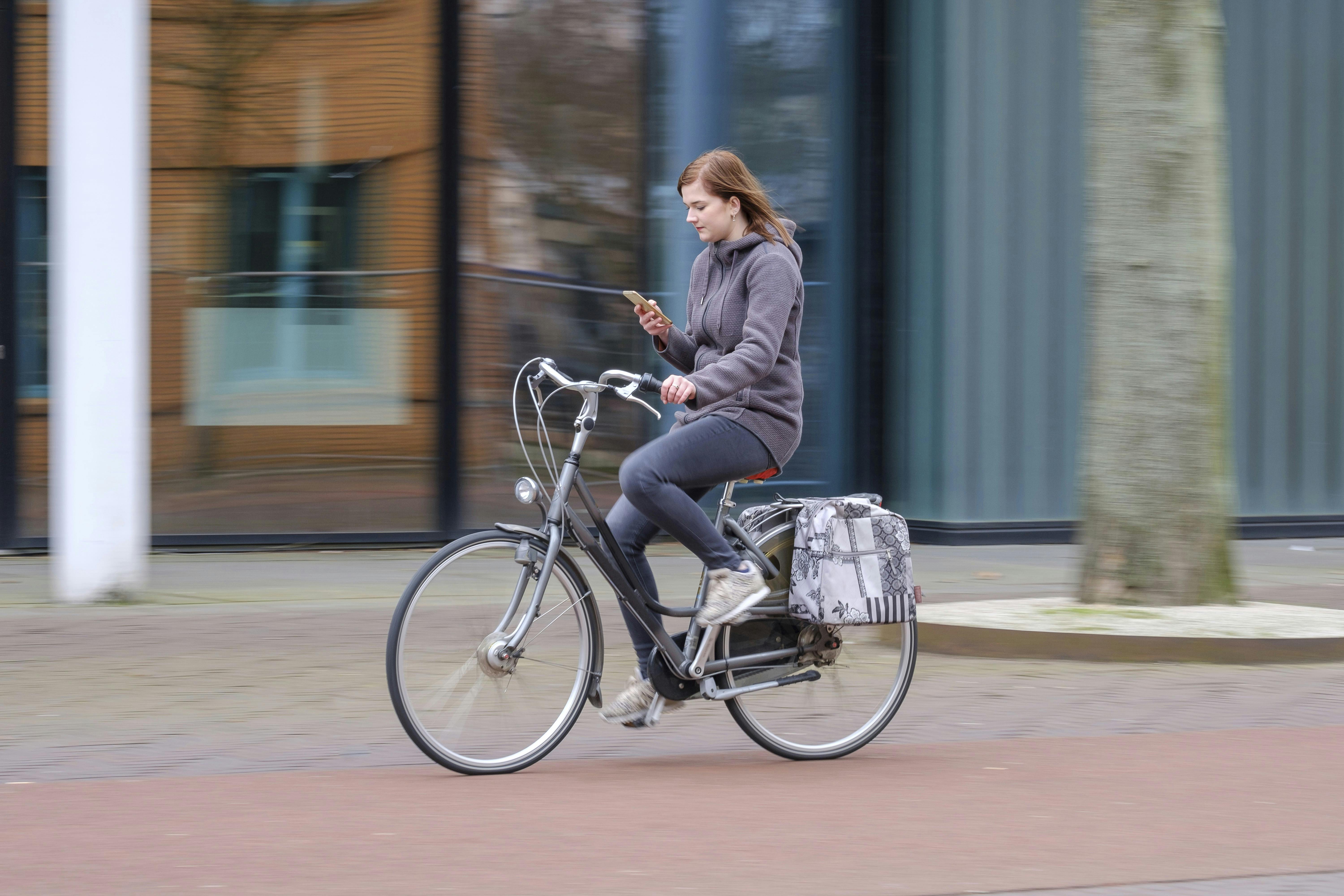 Young woman getting distracted by his smartphone while riding his bicycle around the city